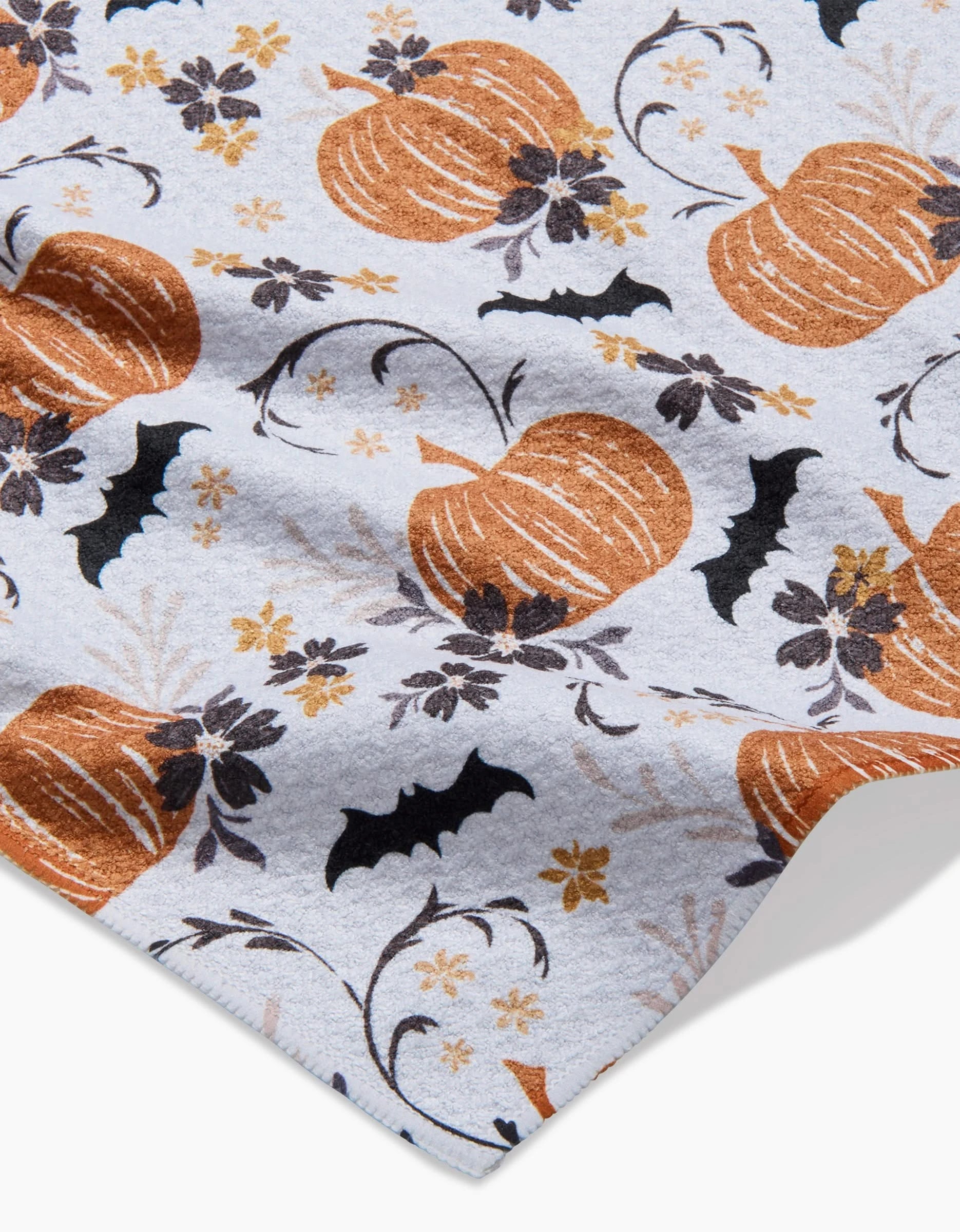 The Bats In The Pumpkin Patch kitchen towel by Ashley Celena is made from recycled material and features a Halloween pattern with orange pumpkins, black bats, and dark flowers on a light background.