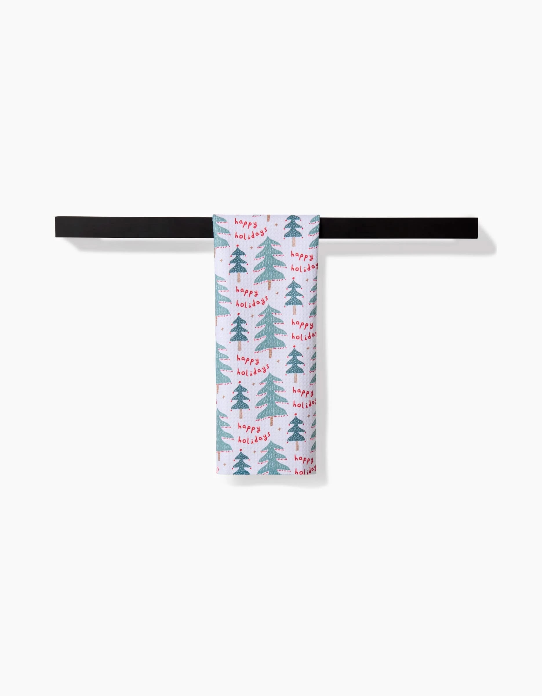 The Roxy Marj Berry Happy Holidays towel, featuring green Christmas trees and red festive text, hangs neatly on a black towel bar against a plain white background.