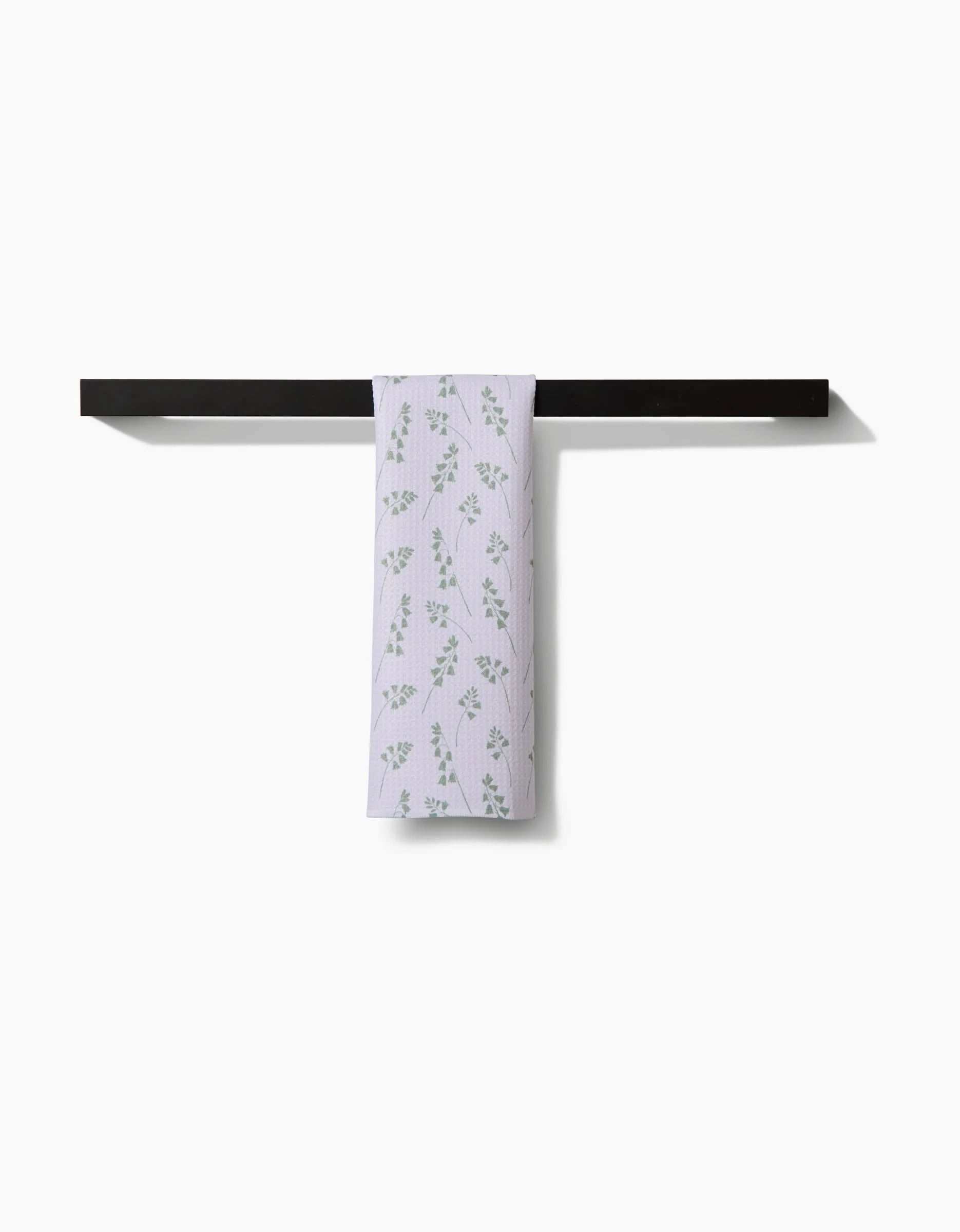 The Linda Fox Blue Bells Green bar towel, featuring a subtle green leaf pattern and crafted from Geoweave fabric, is draped over a black towel bar against a plain white background.
