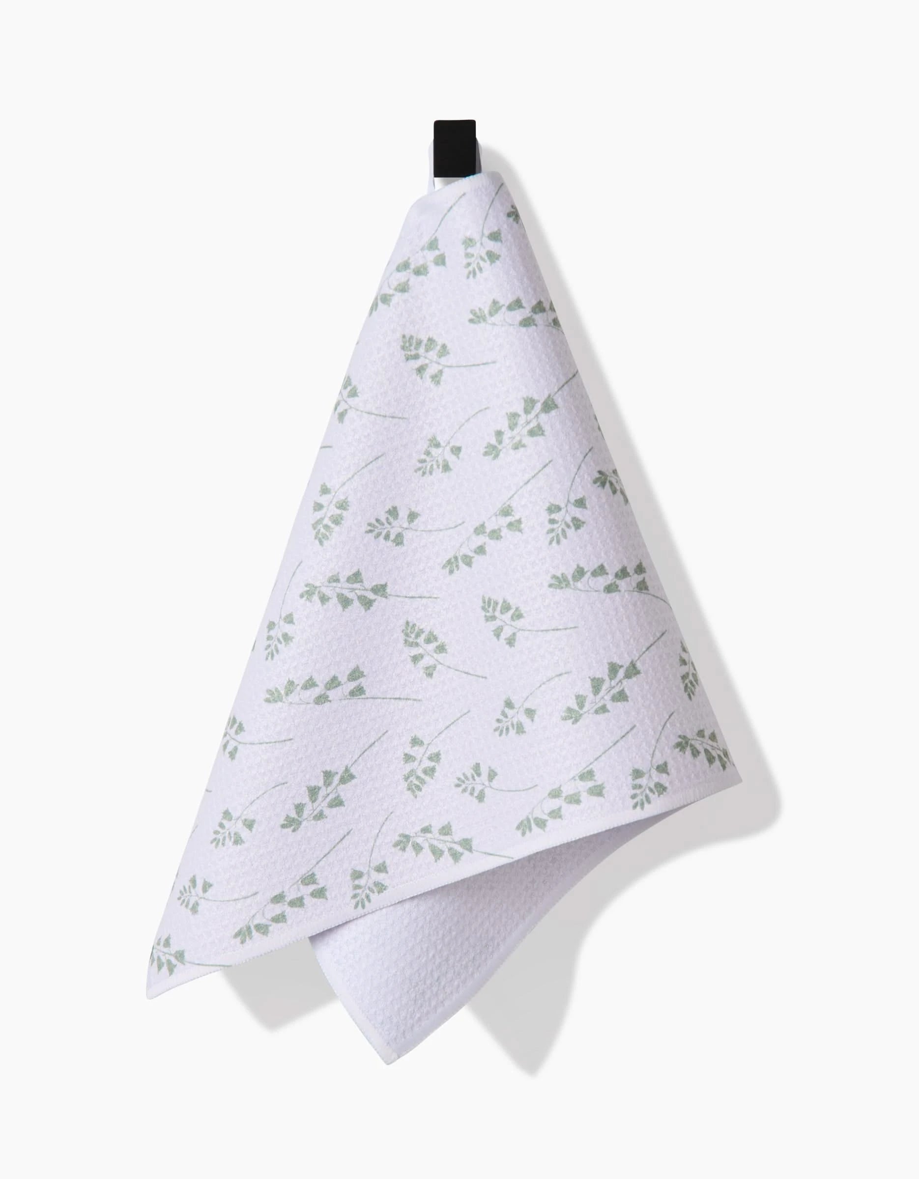 The Linda Fox Blue Bells Green Bar Towel, made from Geoweave fabric and featuring a subtle green leaf pattern, hangs from a black loop against a plain white background.