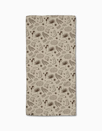 The Geometry Bonfire Nights bar towel is beige and rectangular, made from Geoweave fabric with a dark brown repeating pattern of hands, books, stars, speech bubbles, musical notes, and abstract shapes.