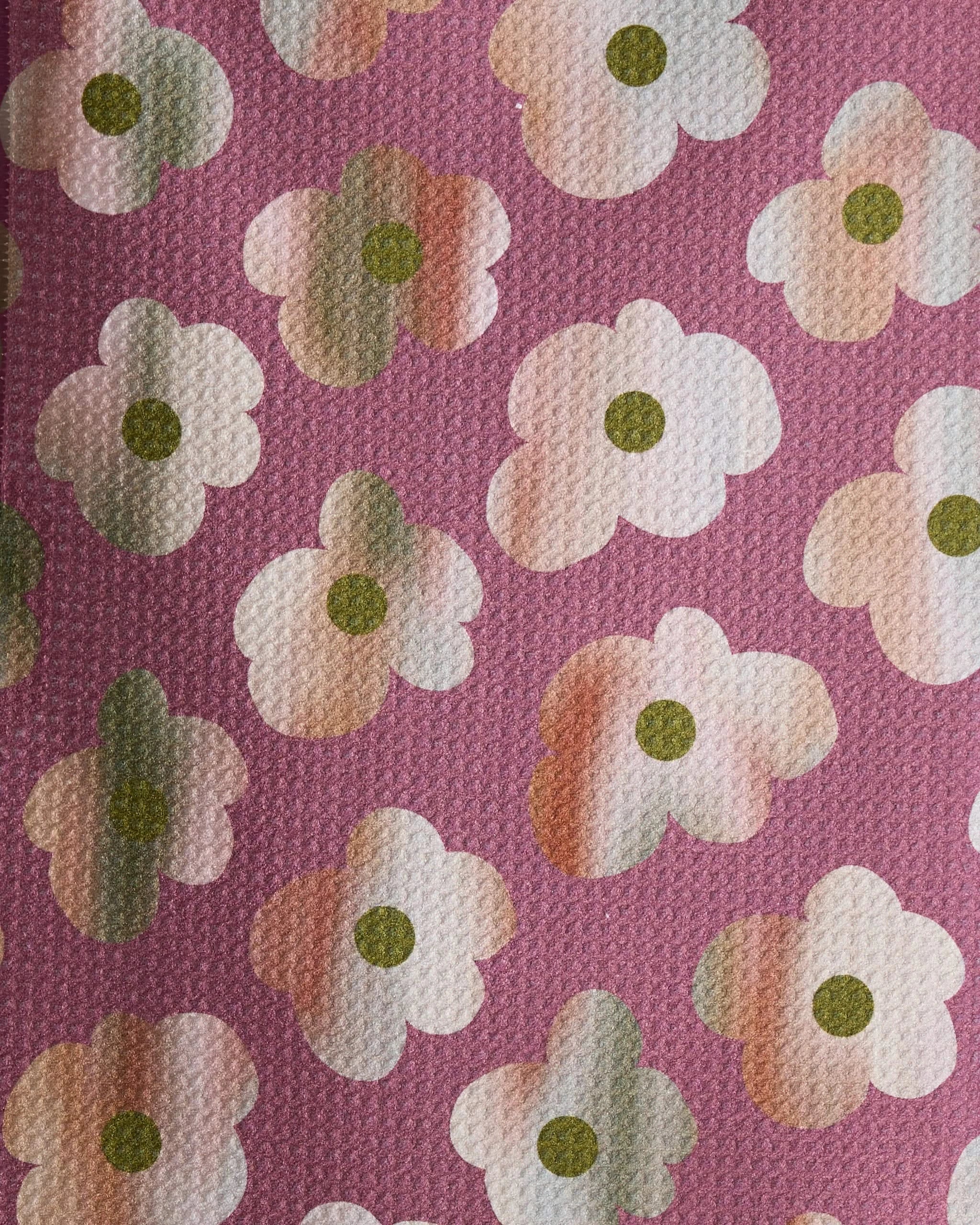 A close-up of Geometrys Brushed Bouquet, featuring a pink background with white stylized flowers, green centers, and light brown accents in an ultra-absorbent bar towel-inspired pattern.