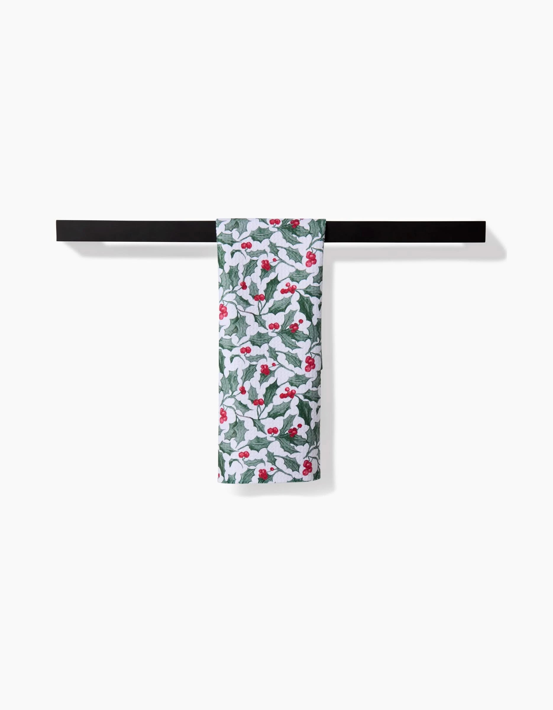 The Aubrey Fairchild Christmas Mistletoe towel, featuring festive green leaves and red berries, hangs neatly on a black bar holder against a white background.