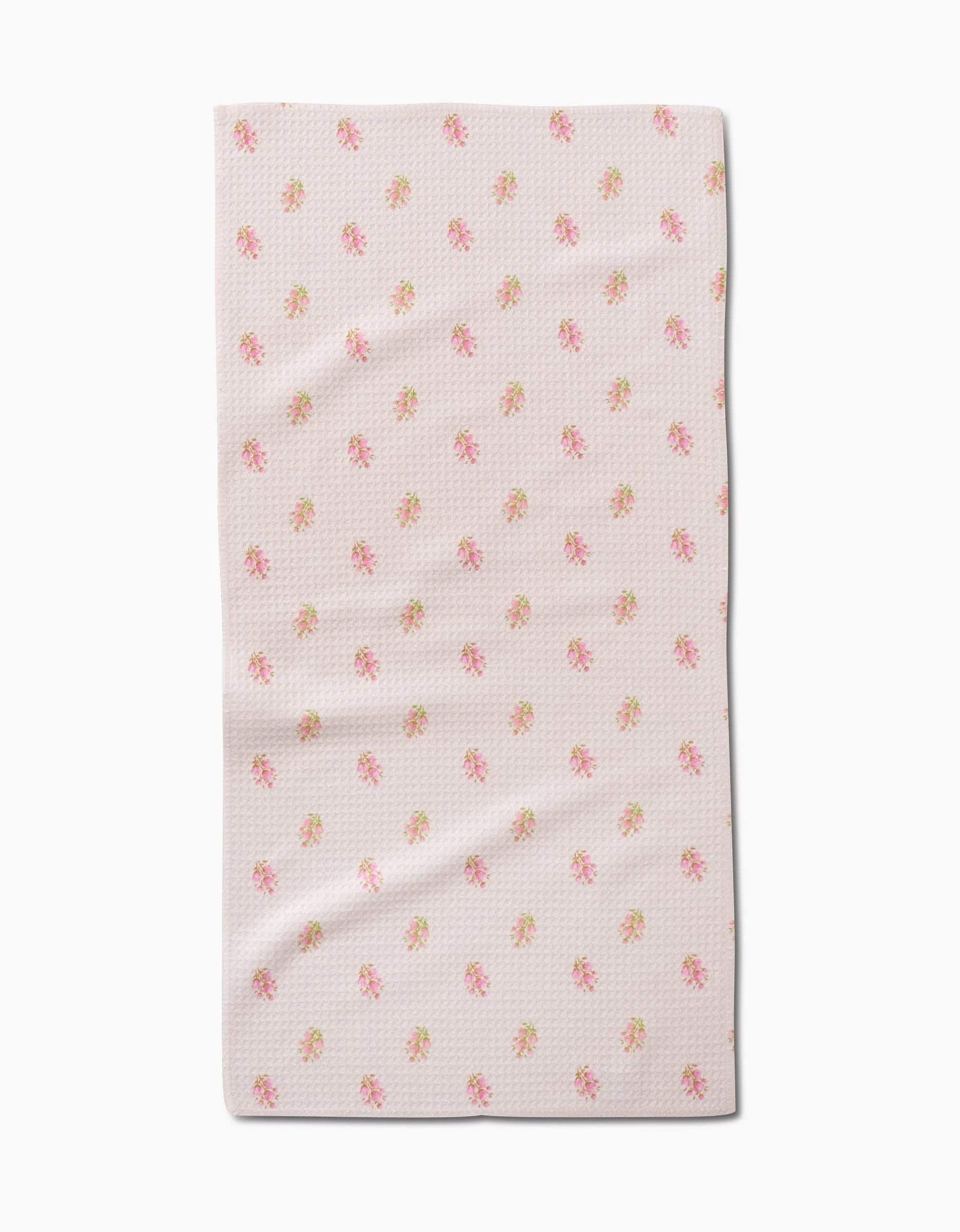 The Cindy bar towel by Kelsi Fullmer features light pink fabric with a subtle textured pattern and scattered pink and yellow floral prints. Made from recycled materials, the towel is shown flat on a white background with gentle folds.