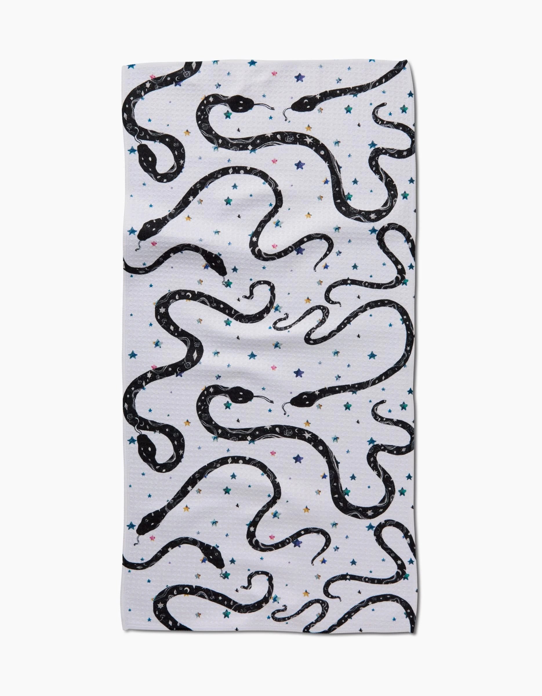 The Cosmic Snakes bar towel by Pascale Dilger features black snakes and blue, yellow, and pink stars scattered across its white Geoweave™ fabric.