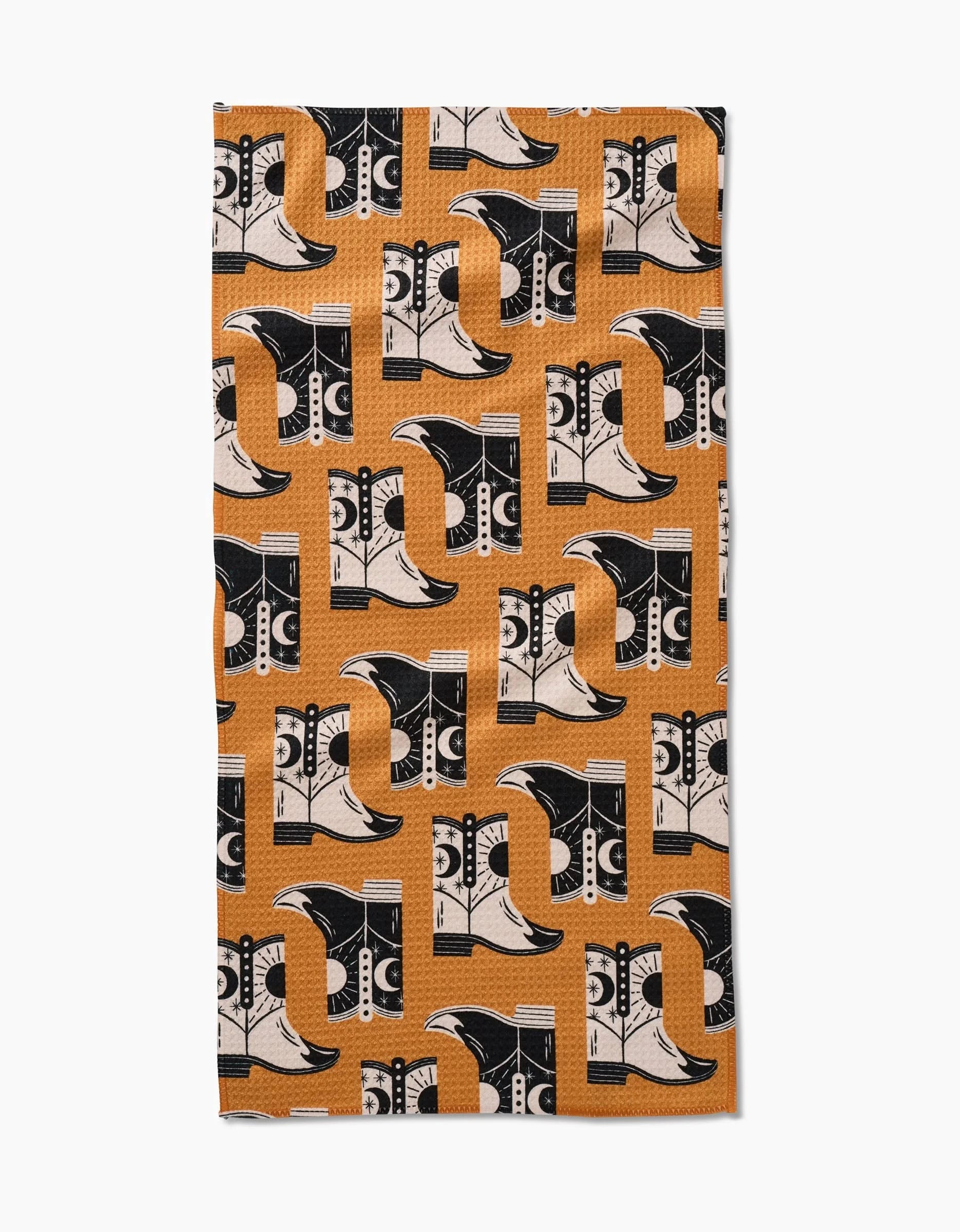 The Megan Roy Cowboy Boots rectangular bar towel features a geometric pattern of stylized cowboy boots in black, cream, and orange on a textured orange background. Made from ultra-absorbent recycled materials with alternating boot orientations.