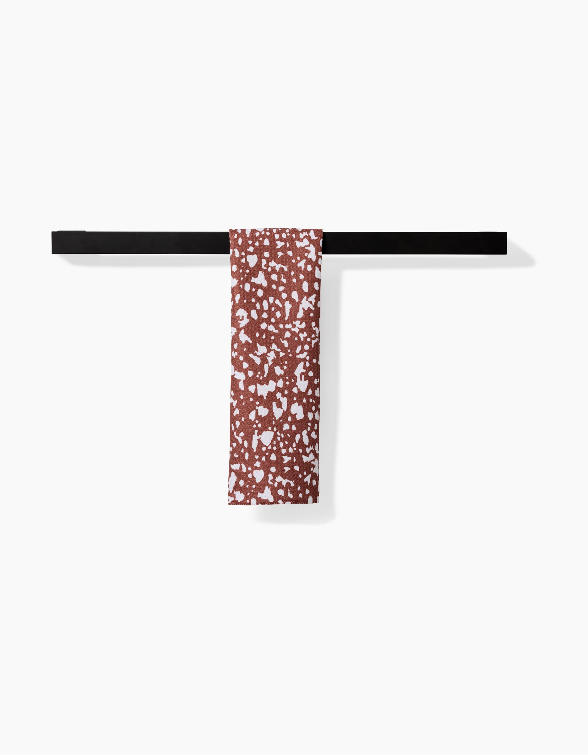 A black horizontal bar holds Hufton Studio’s Cowboy Horse Hide Bar Towel, made from recycled materials and featuring a white speckled pattern on a reddish-brown background, displayed against plain white.