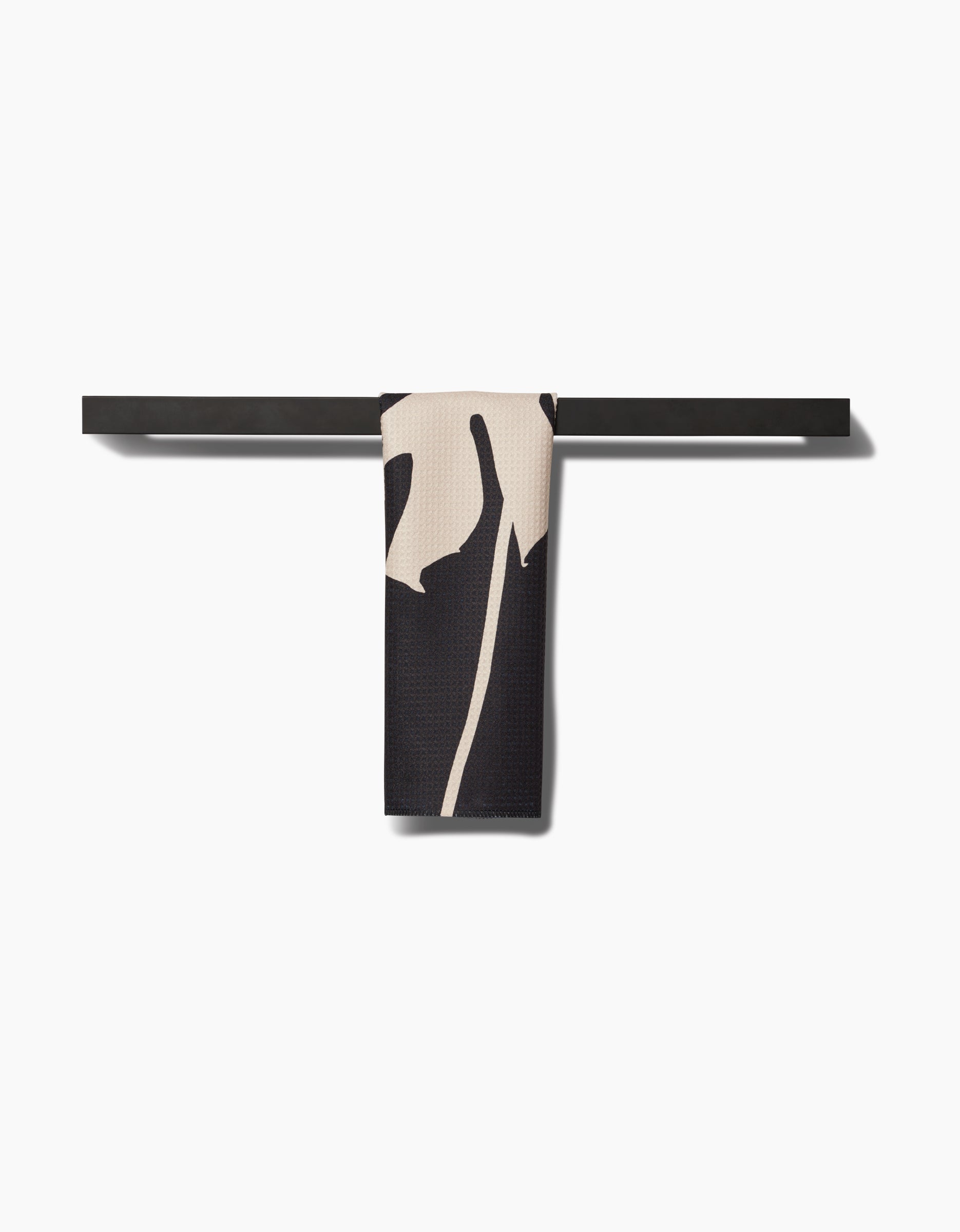 The PrintedPlant Cream Monstera bar towel, featuring a black and cream pattern and crafted from Geoweave fabric, hangs neatly over a sleek horizontal black bar against a plain white background.