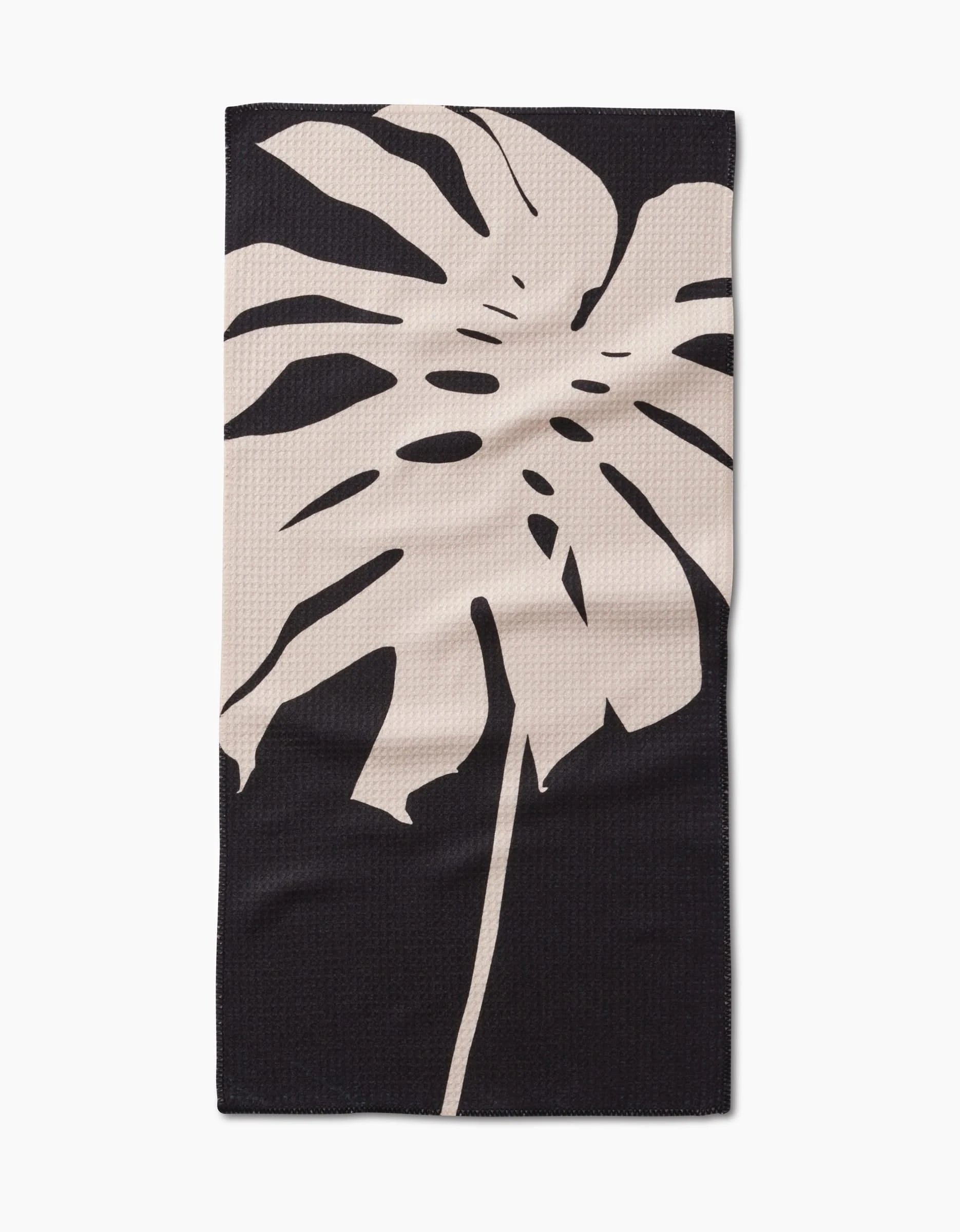 The Cream Monstera Bar Towel by PrintedPlant features a large beige monstera leaf on dark Geoweave fabric, offering superior absorbency and style.