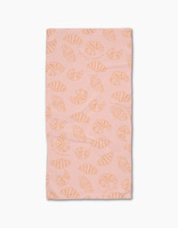 The Croissant Crush towel by Geometry is a pink rectangular bar towel with an all-over orange line-drawn croissant pattern, crafted from durable Geoweave fabric and displayed on a white background.
