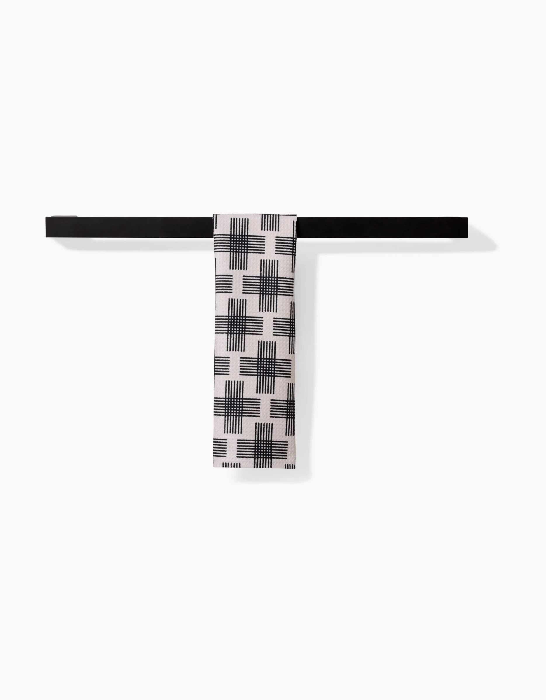 A black horizontal bar holds a folded white Bar Towel—Cross Hatch by Rosa Kichline. Made of Geoweave fabric, the towel displays a black geometric grid and line pattern against a plain white background.