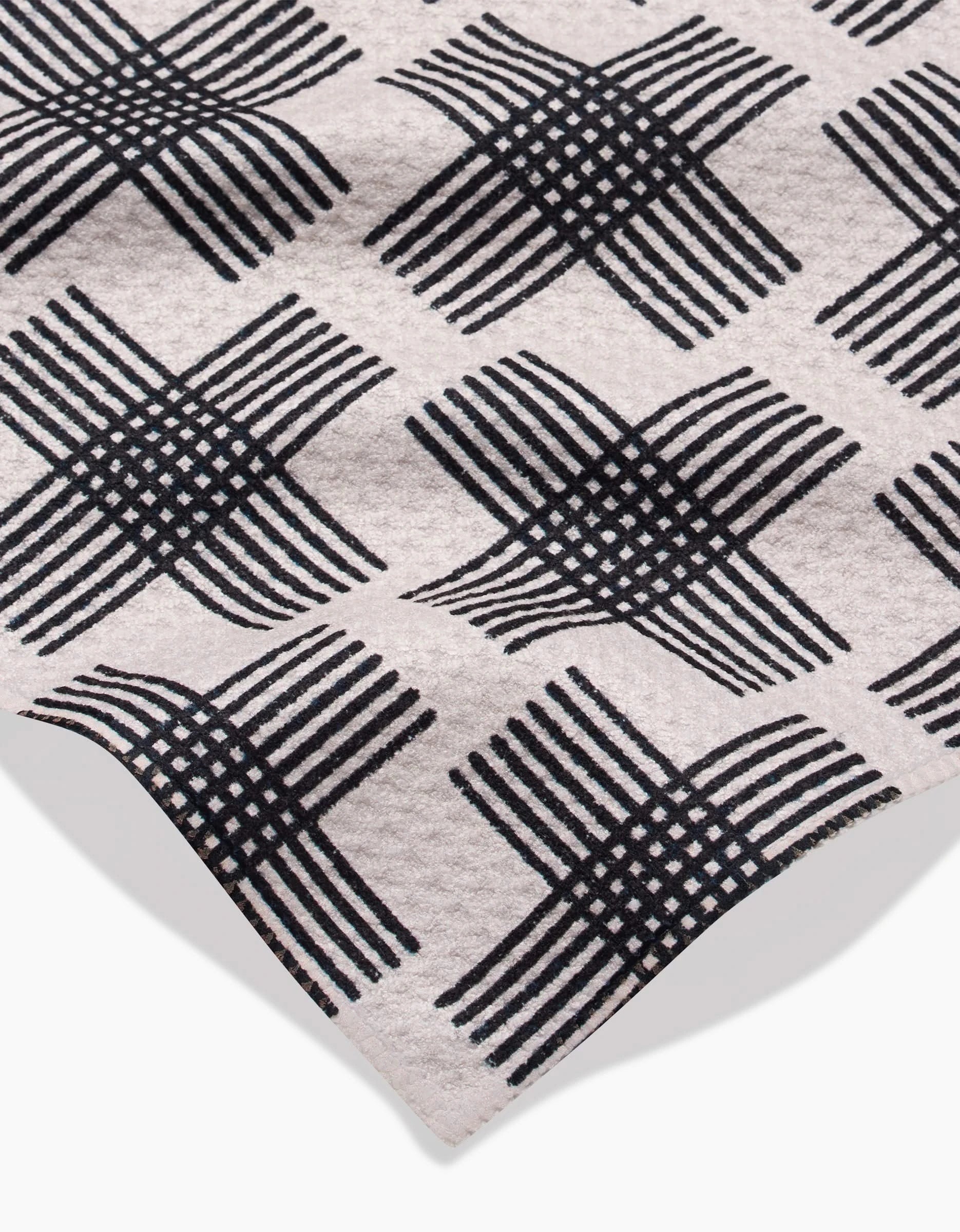 A close-up of Rosa Kichline’s Cross Hatch bar towel in beige Geoweave fabric, featuring a black diamond-patterned crisscross design. Made from post-consumer recycled materials with a folded corner and subtle texture.