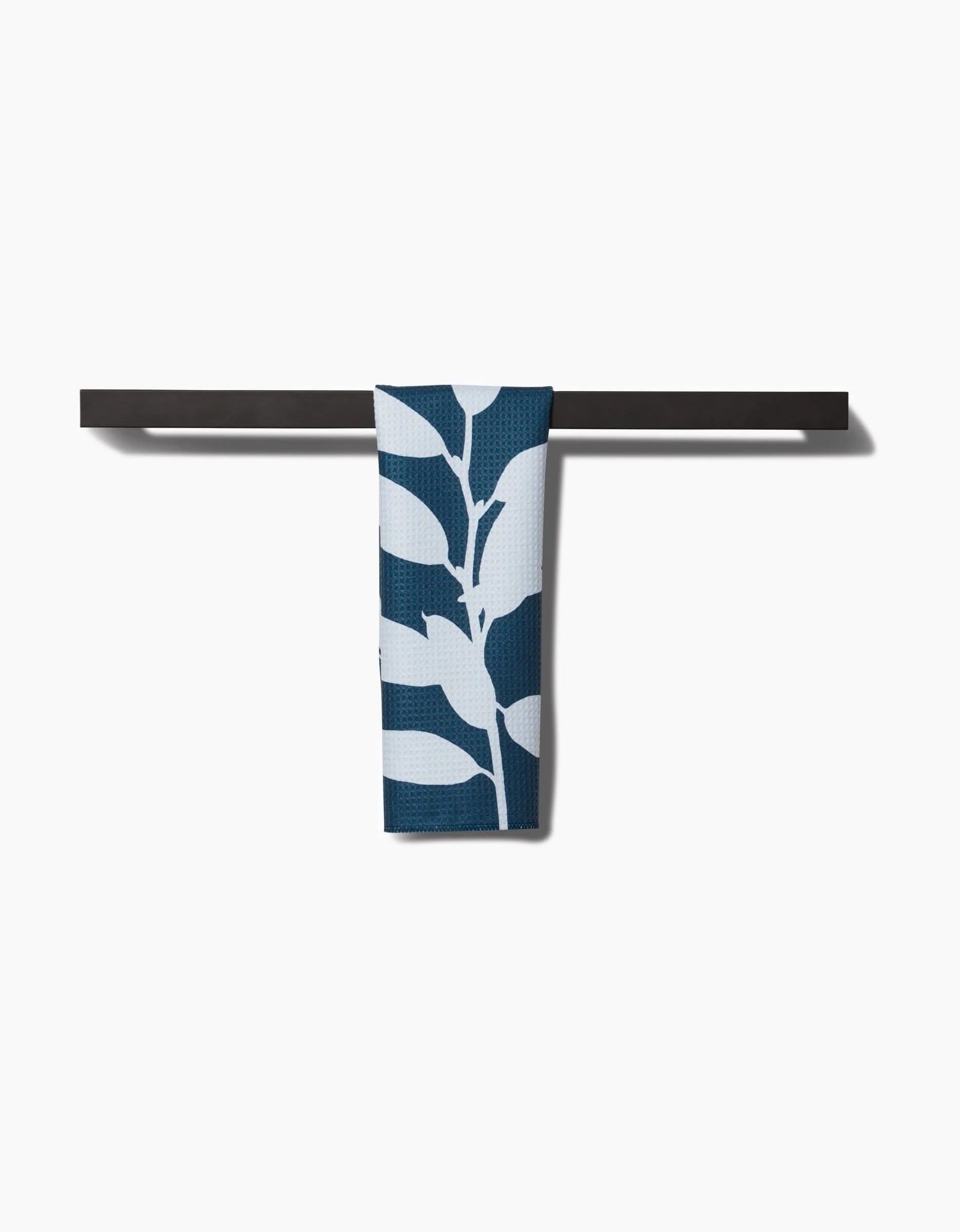 The Doghobble bar towel by PrintedPlant, featuring a bold blue and white leaf design on Geoweave fabric, is displayed neatly over a sleek black towel bar against a plain white background.