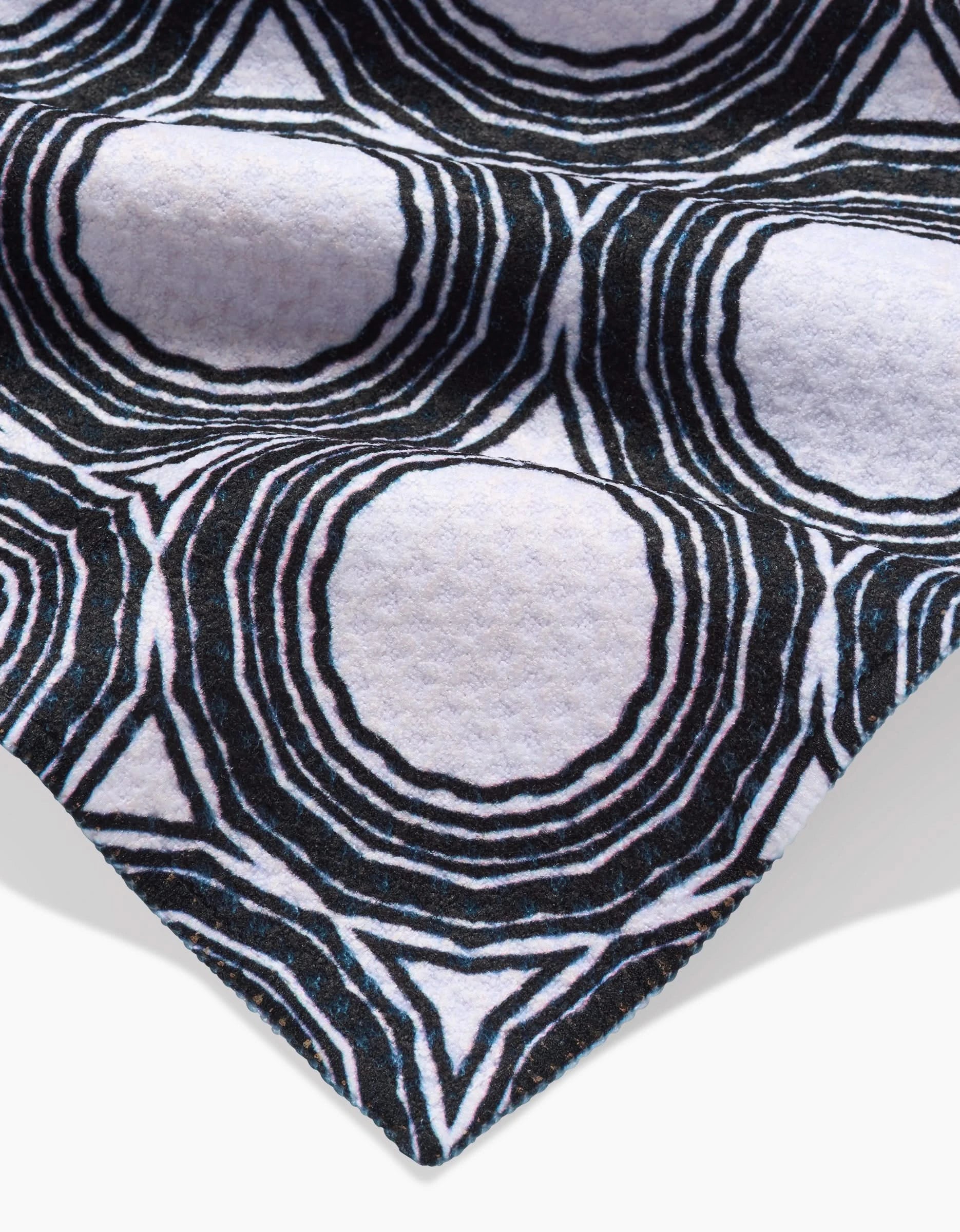 A close-up of Dosido by Katherine Berkeley shows its Geoweave fabric in a black and white concentric circular pattern, giving a textured, almost 3D look. The edge of this ultra-absorbent bar towel is visible in the lower corner.