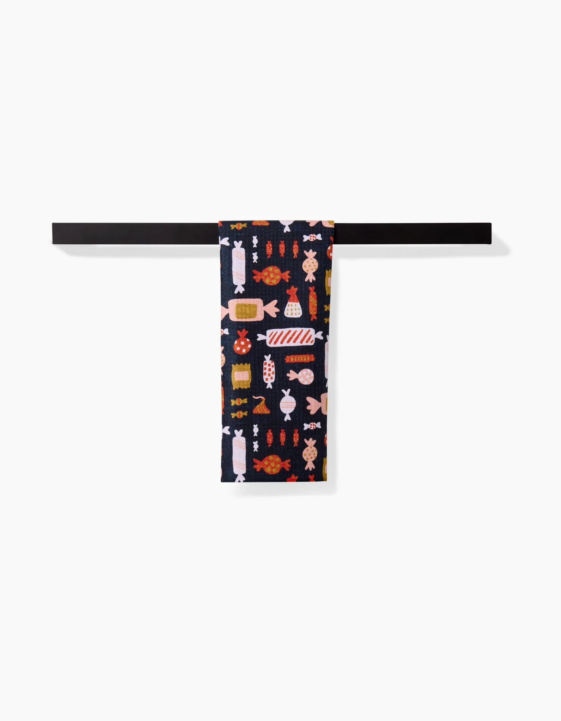 The Edwina towel by Amy MacCready, featuring colorful candy wrapper designs on ultra-absorbent dark fabric, hangs neatly over a simple horizontal black towel bar against a plain white background.