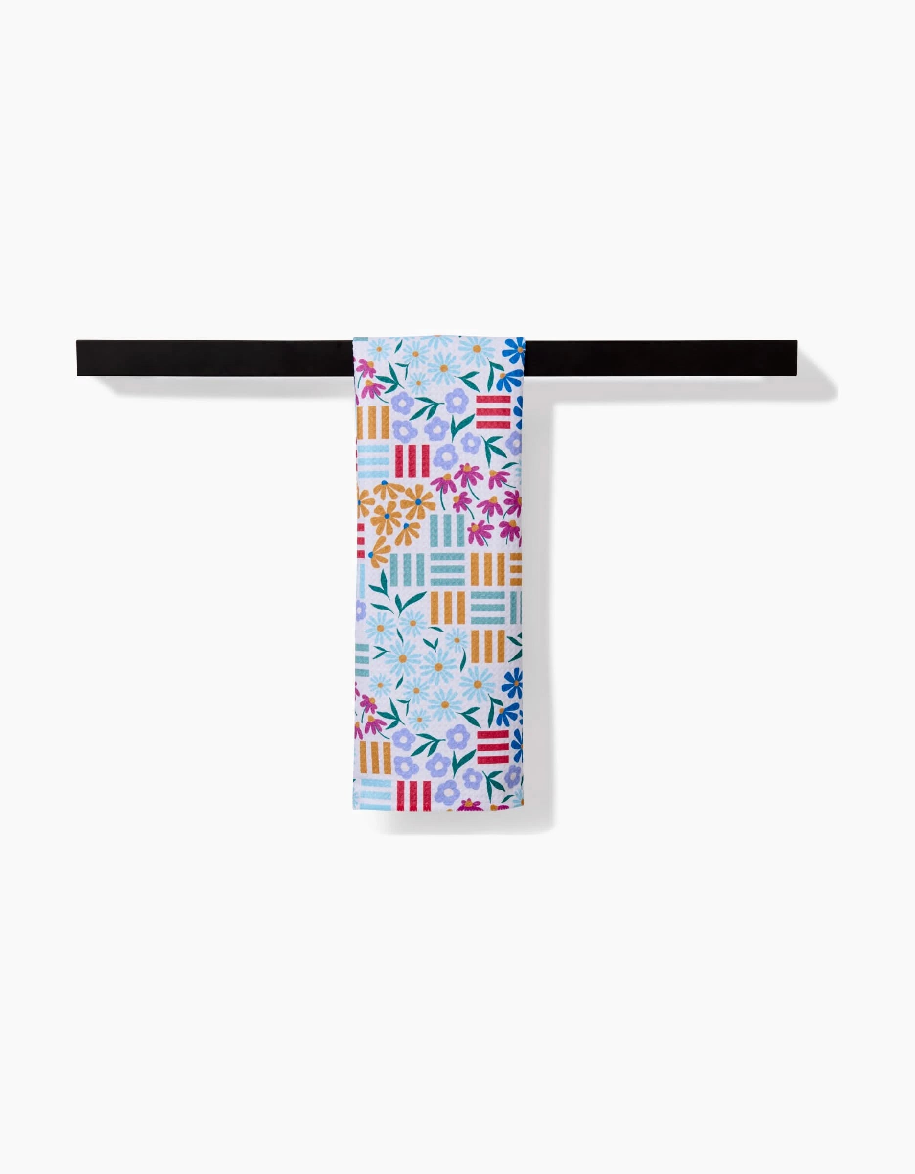 The Floral Garden bar towel by Charlie Rowan Designs features vibrant floral and geometric patterns in blue, orange, pink, and yellow on soft Geoweave fabric, bringing lively color to your space when hung on a black towel bar.