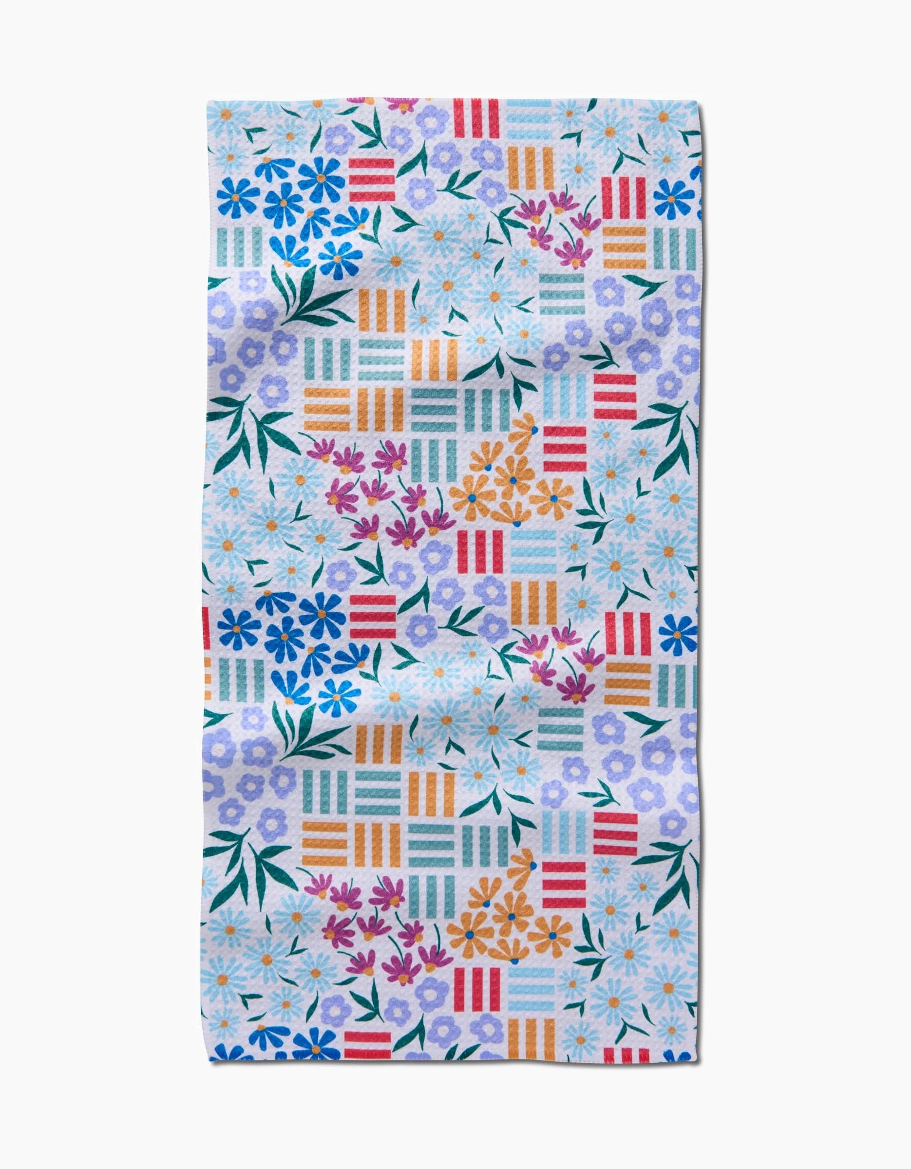 The Floral Garden Bar Towel by Charlie Rowan Designs features a colorful floral and geometric pattern on Geoweave fabric, with blue, purple, white, and red flowers, green leaves, and multicolored stripes on a light background.