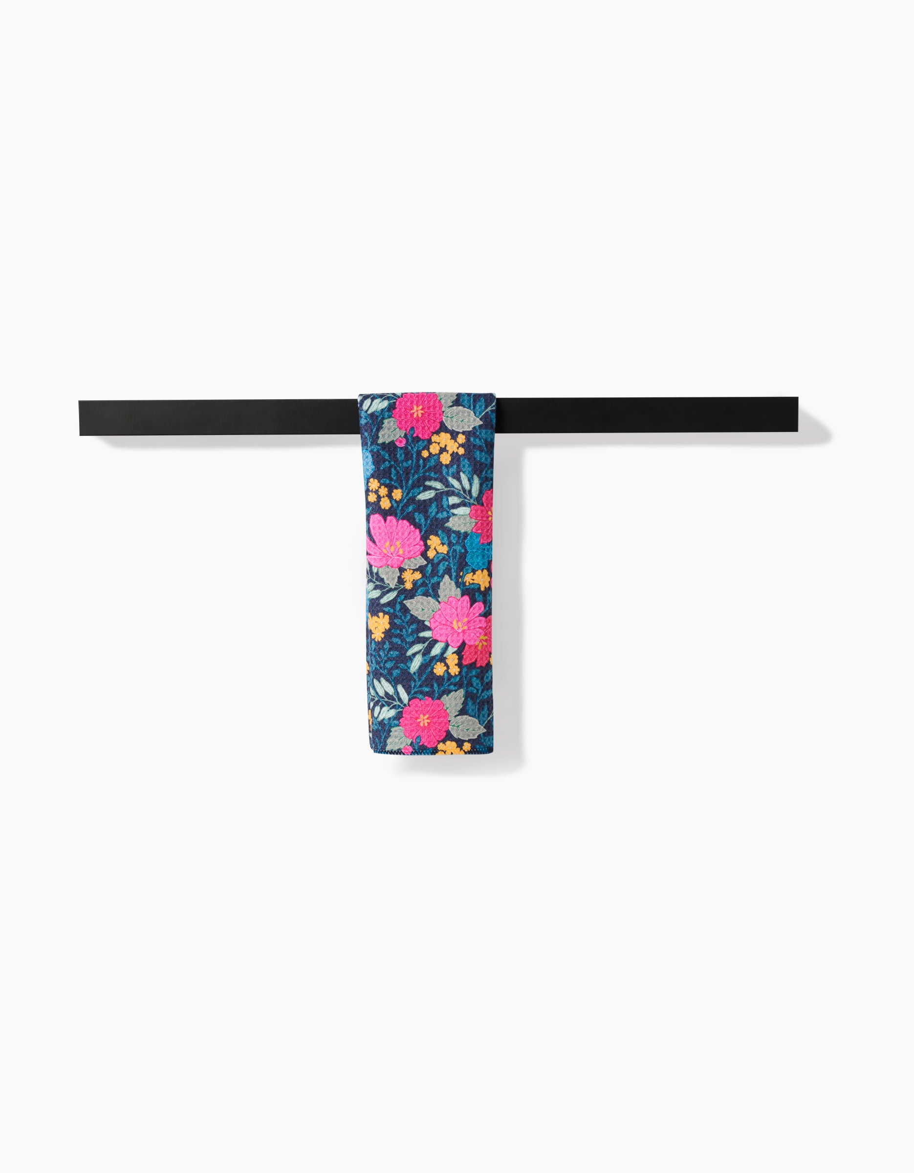 A dark bar displays the folded Flower Bouquets bar towel by Katie OShea, featuring a vivid pink, yellow, and orange floral pattern on white Geoweave fabric. The minimalist scene is set against a plain white backdrop.