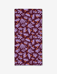 The Flower Pop napkin by Elisabeth Wing is a rectangular cloth made from recycled materials, featuring a dark purple background with light purple daisies and orange centers scattered across the surface.