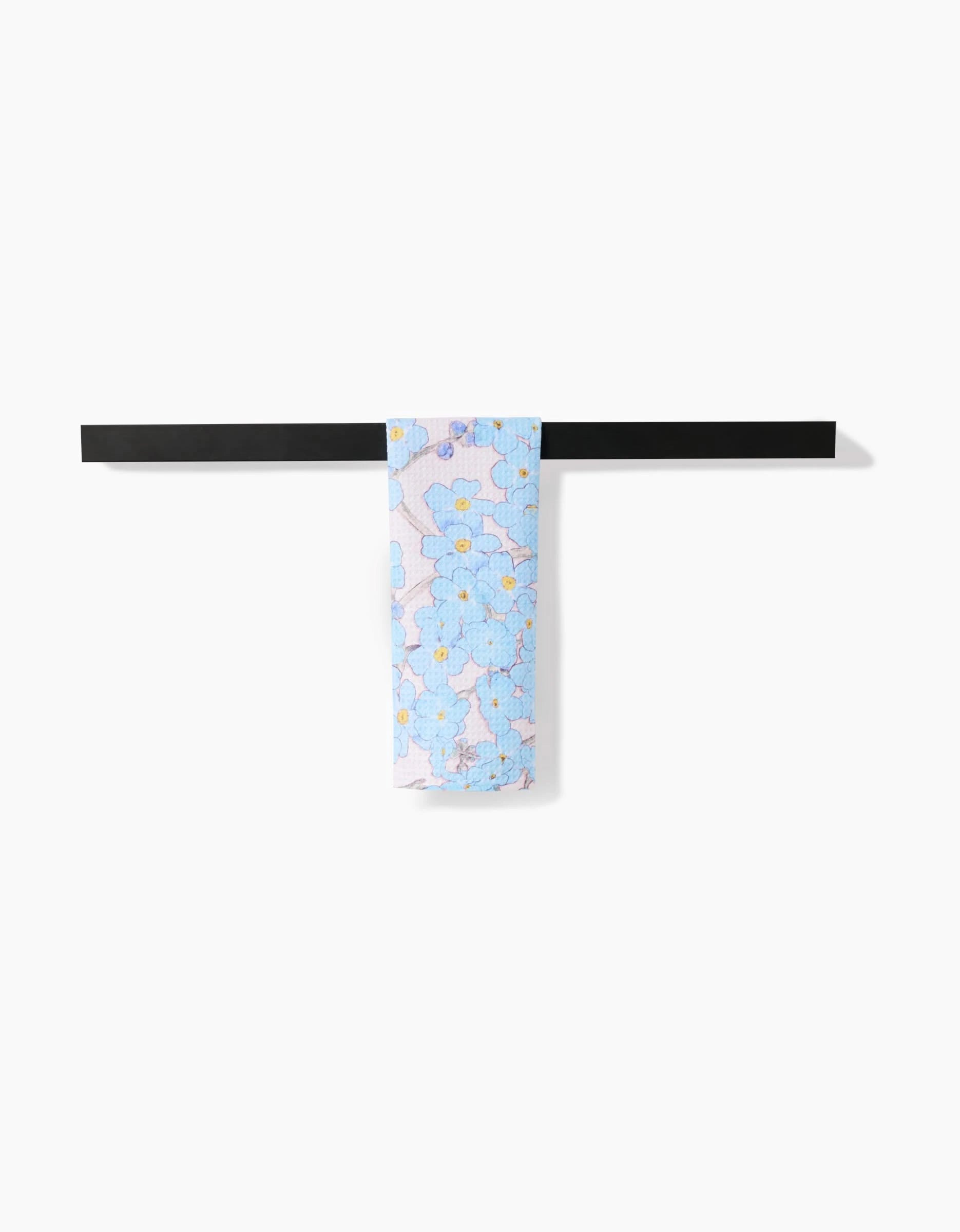 The Pascale Dilger Forget Me Not Floral light blue scarf, crafted from recycled materials and featuring a floral design, is draped neatly over a sleek black rod against a plain white background.