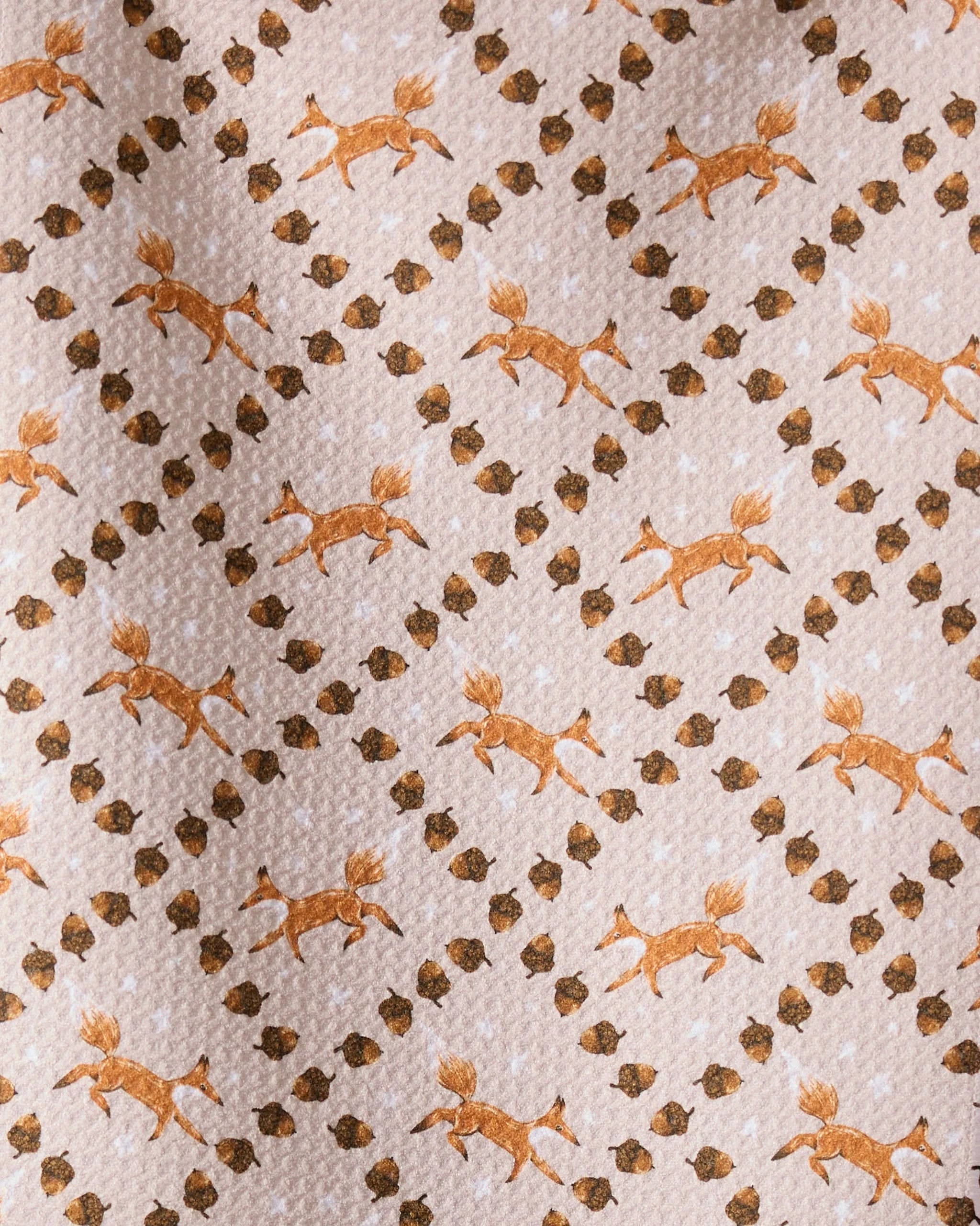 The Geometry Foxes and Twinkles bar towel showcases orange running foxes and brown twinkles in a diagonal grid on light beige, crafted from recycled materials.