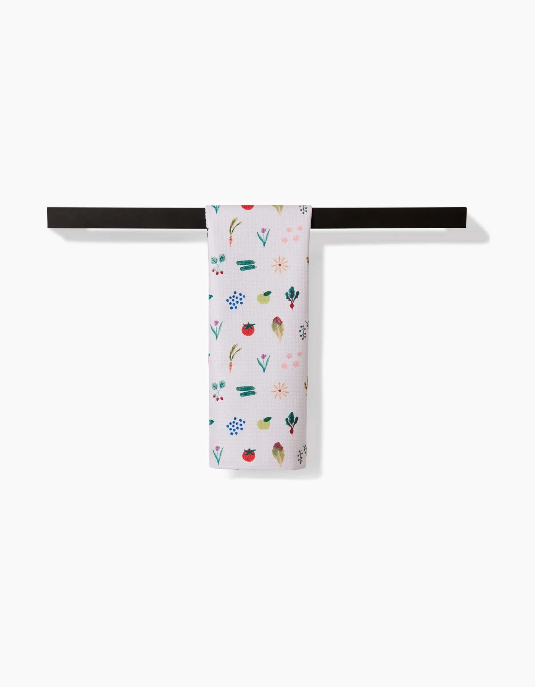 The Brittany Jepsen Fresh Produce dish towel, made from ultra-absorbent Geoweave fabric and featuring colorful floral and leaf patterns, hangs neatly on a black rod against a plain white background.