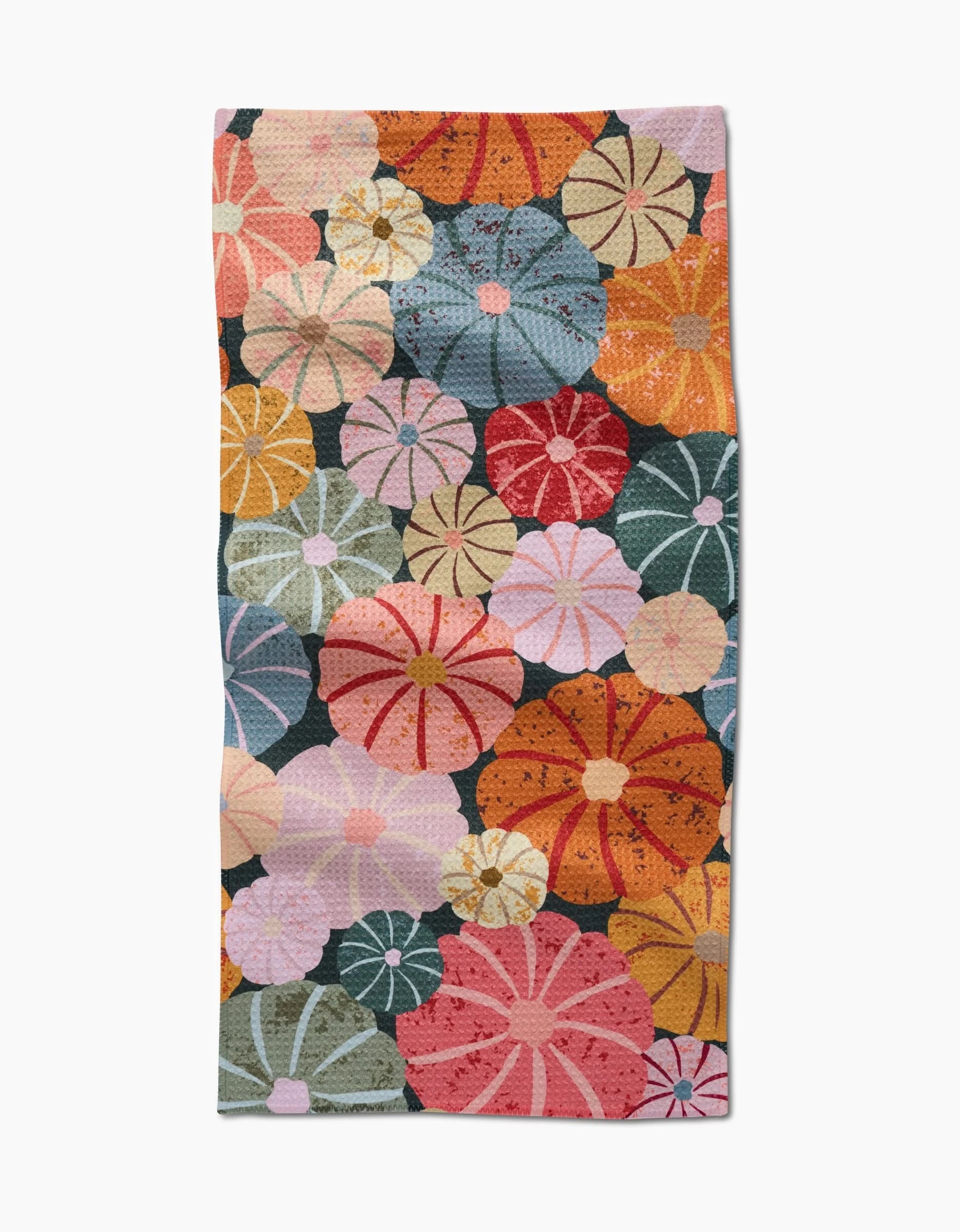 The Gorgeous Gourds towel by Rebecca Bobko is ultra-absorbent and features a vibrant pattern of overlapping, stylized flowers in orange, red, pink, yellow, blue, and green on a dark background.