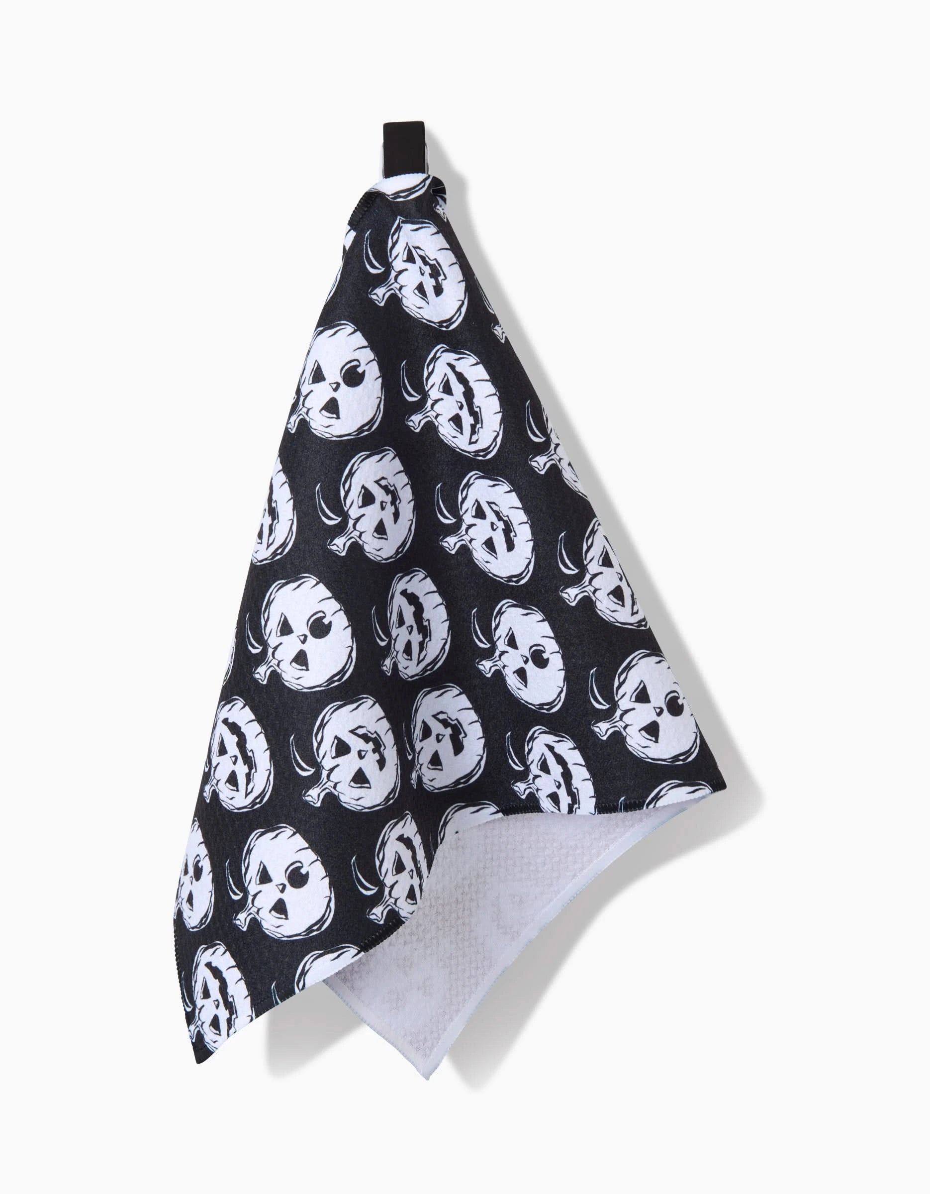 A black ultra-absorbent kitchen towel by Aubrey Fairchild, named Halloween Pumpkins, hangs from a hook and features a repeating white pattern of stylized pumpkin faces across its surface.