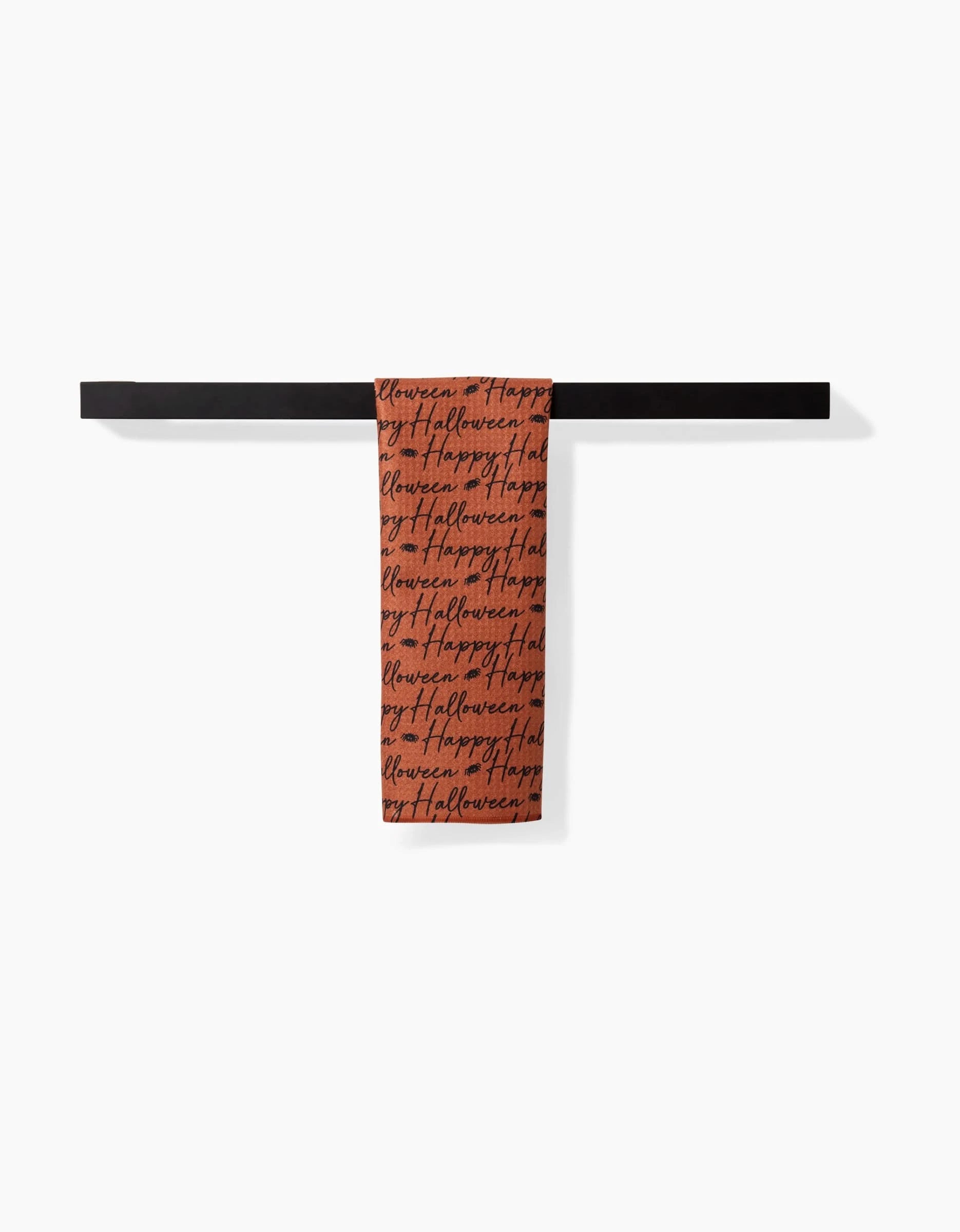The Geometry Halloween Script Orange towel features ultra-absorbent fabric and repeating black Happy Halloween cursive text, shown hanging neatly on a black bar against a white background.