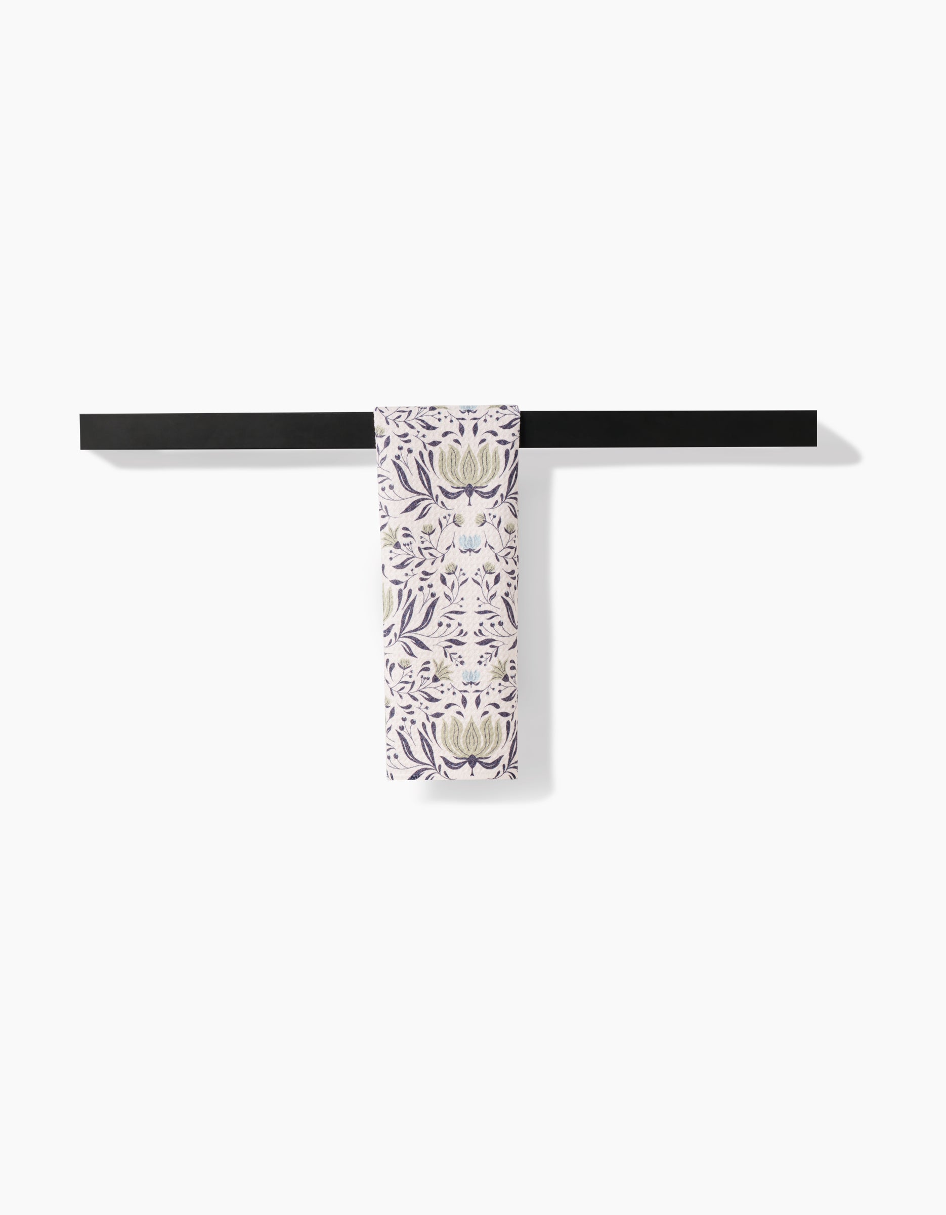The Hello Flowers bar towel by Amita Nair, featuring a purple and green floral pattern on ultra-absorbent Geoweave fabric, is folded and draped over a black bar against a white background.