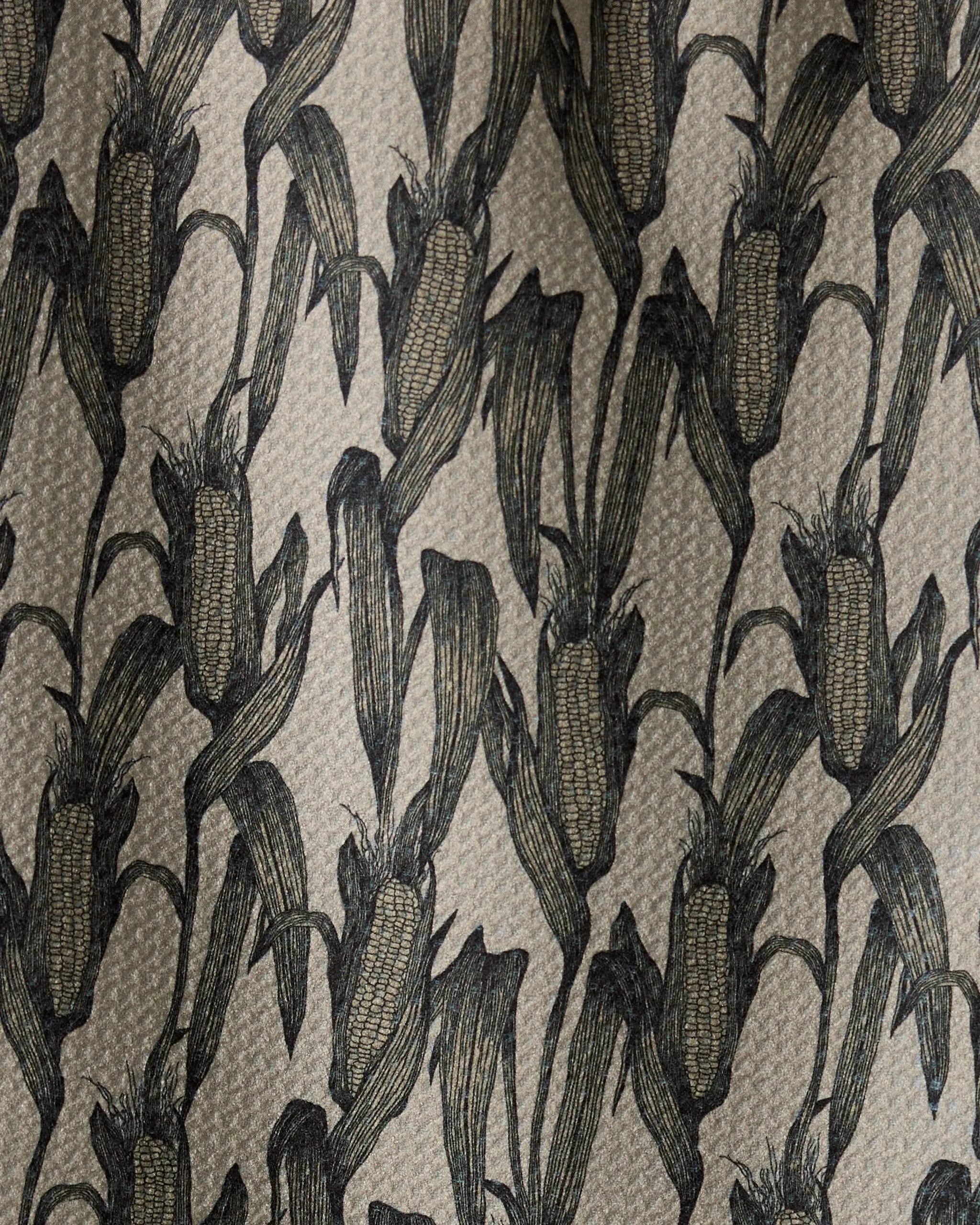 Close-up of Husk, a bar towel by Geometry, featuring a repeating pattern of black corn cobs and leaves on a beige background. The illustration-style design highlights intricate details. Made from recycled materials.