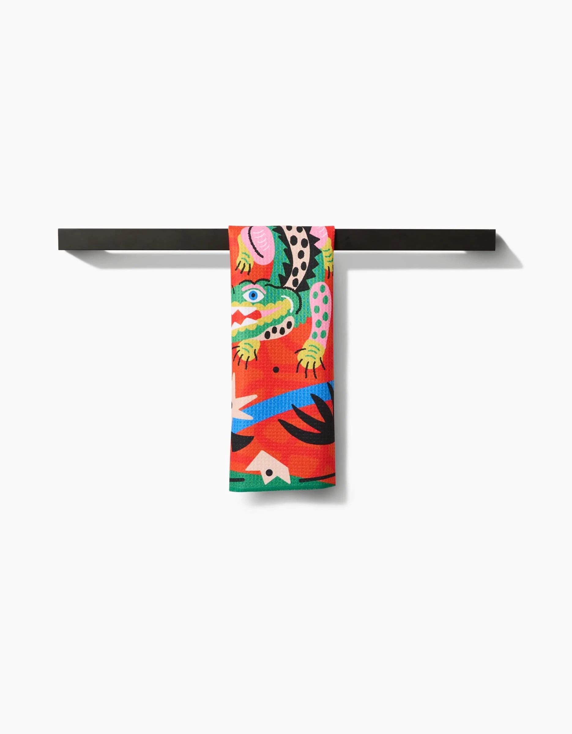 The Jacaré bar towel by Camila Leão features colorful abstract animal and geometric designs in green, pink, blue, and black. Made from sustainable post-consumer recycled materials, its shown draped on a minimalist black metal towel bar.