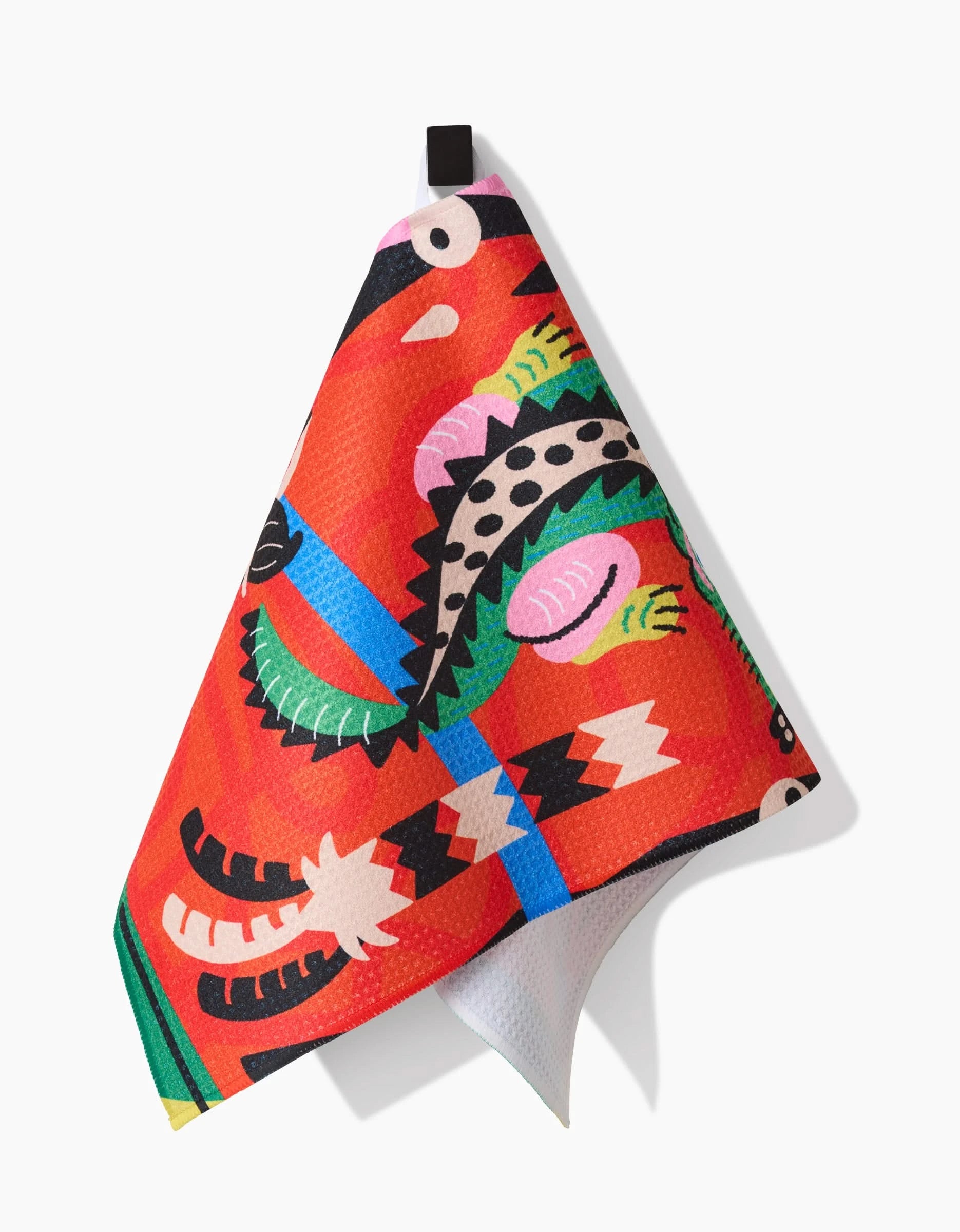 The Jacaré bar towel by Camila Leão, crafted from Geoweave fabric, showcases a colorful stylized crocodile and abstract shapes in vibrant red, hanging from a black loop on a white background.