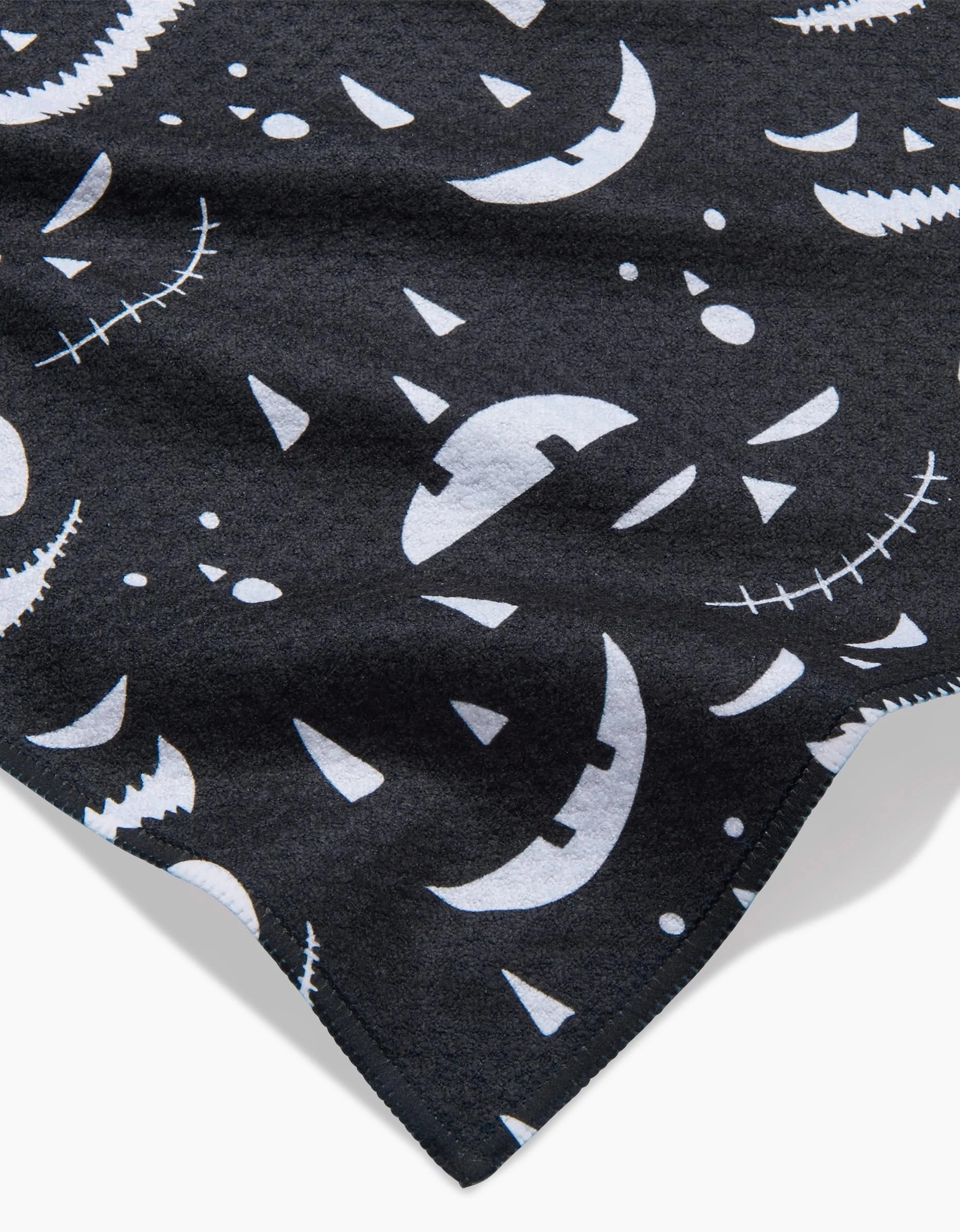 The Danelys Sidron Jack O Lantern Jamboree Black recycled kitchen towel displays white, stylized jack-o’-lantern faces with unique expressions and designs scattered across a black background.