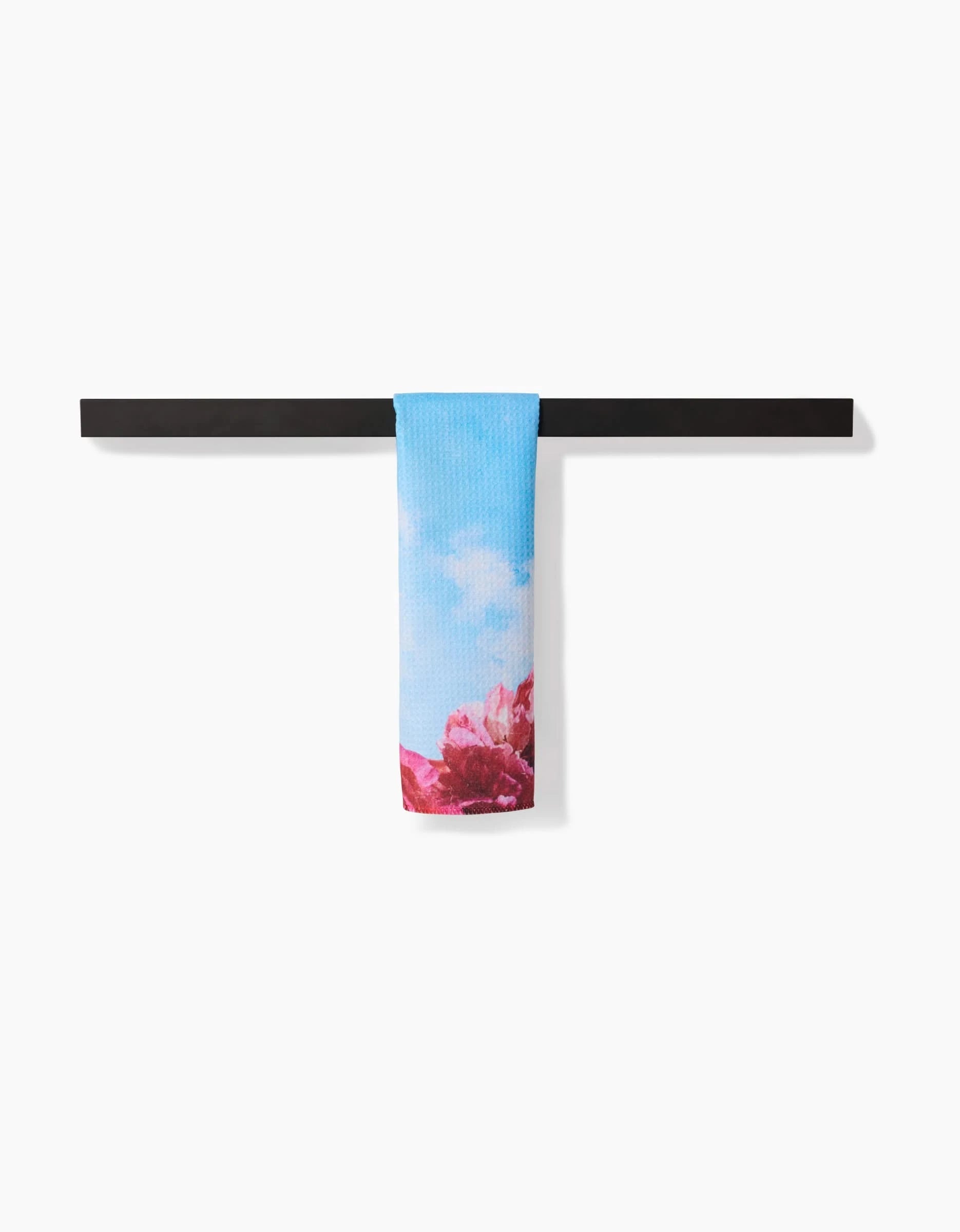 The La Floraison Bar Towel by Stefanie Bales, featuring an ultra-absorbent blue fabric with pink and red floral designs, hangs neatly over a black bar against a plain white background.