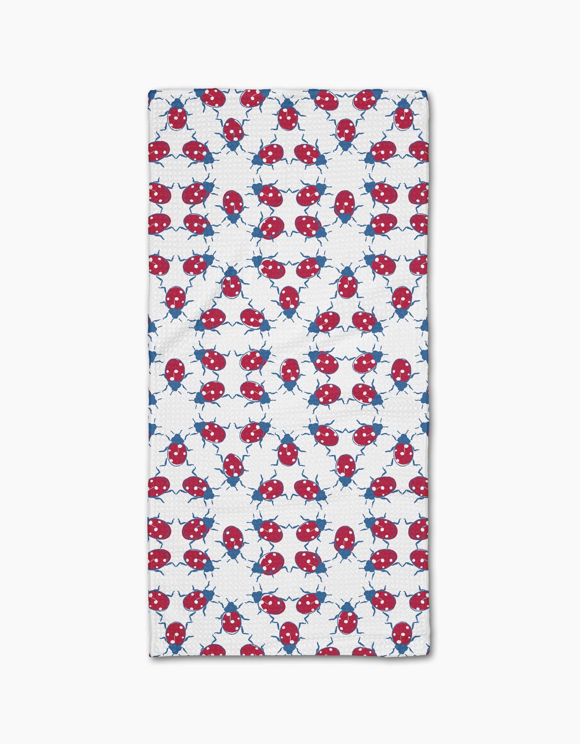 The Ladybug Dance Bar Towel by Second Nature Studio showcases a playful, symmetrical design with red and blue cartoon ladybugs and light blue star shapes on eco-friendly Geoweave fabric.