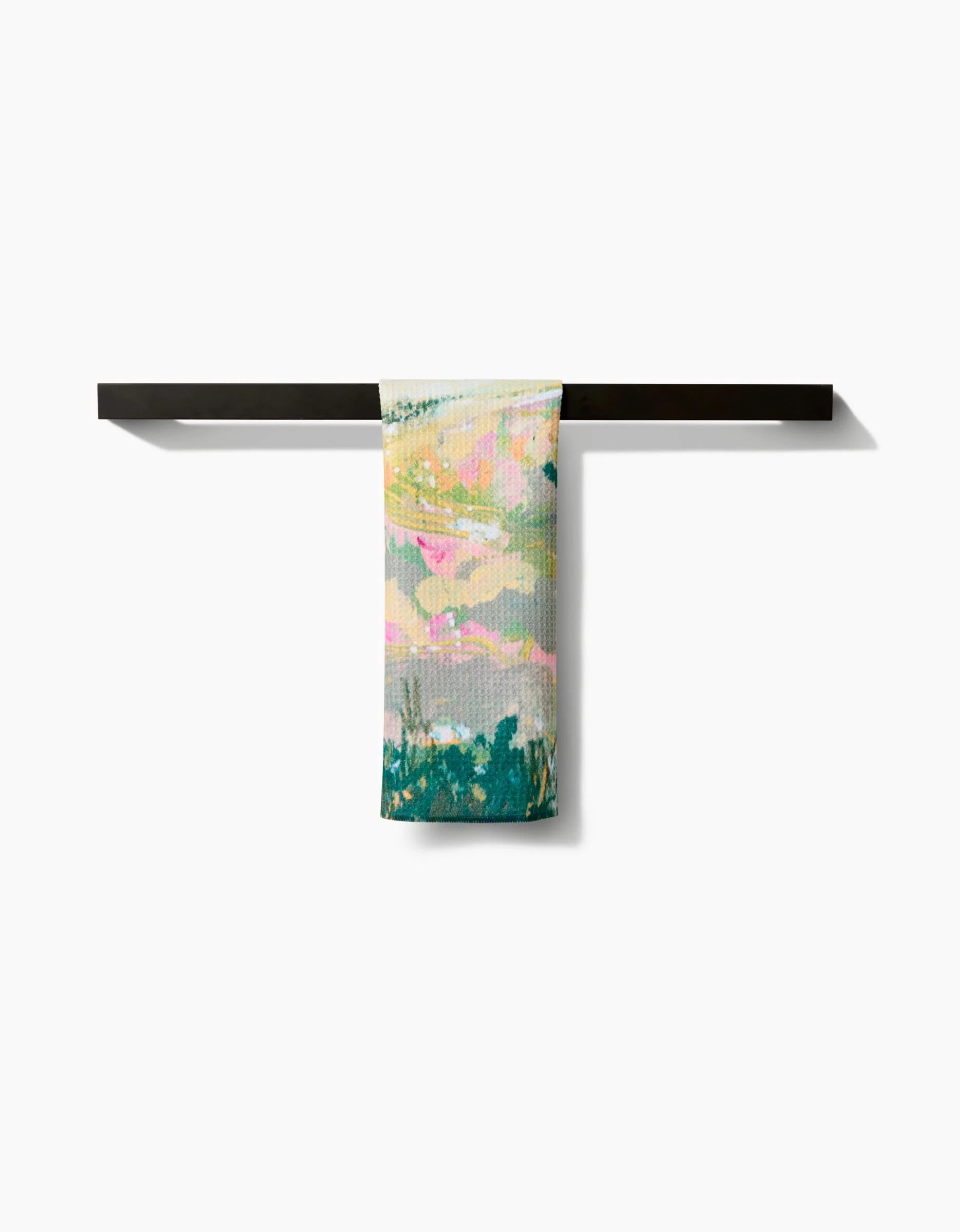 The Land of Milk and Honey Bar Towel by Taryn Brennan, featuring an abstract pastel design and made from recycled materials, is draped over a minimalist black bar set against a plain white background.
