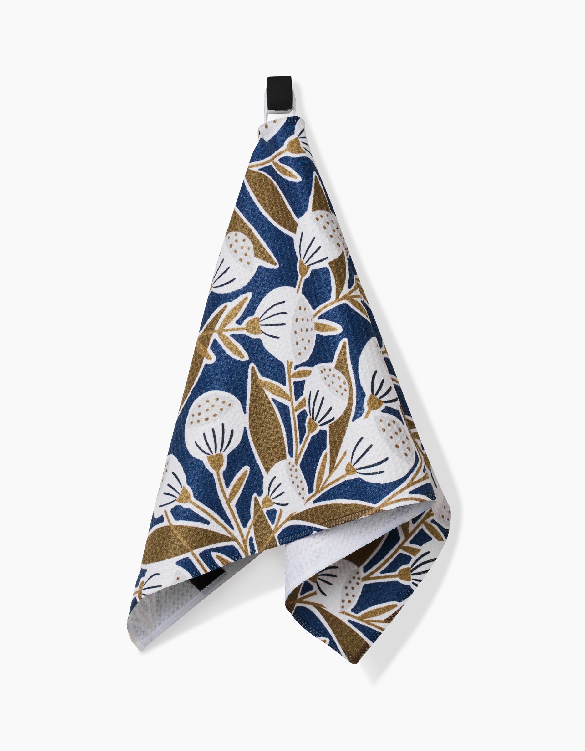 The Leslie kitchen towel by Amy MacCready features ultra-absorbent Geoweave fabric with a white and brown floral pattern on a dark blue background, shown hanging against a plain white surface.
