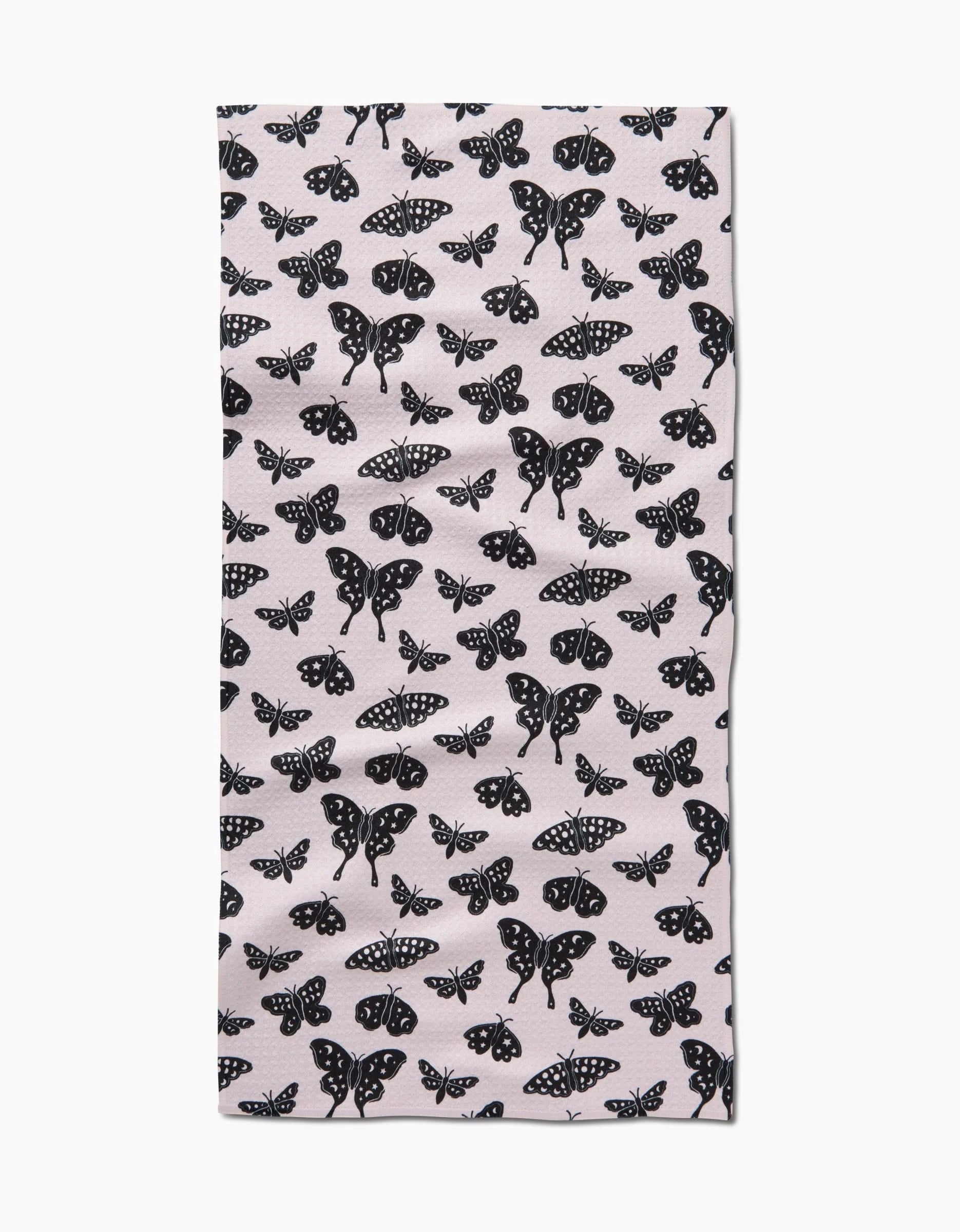 The Kayla Ann Lunar Moths White bar towel is rectangular, made from recycled materials, and features a repeating black moth and butterfly pattern in assorted sizes and wing designs.