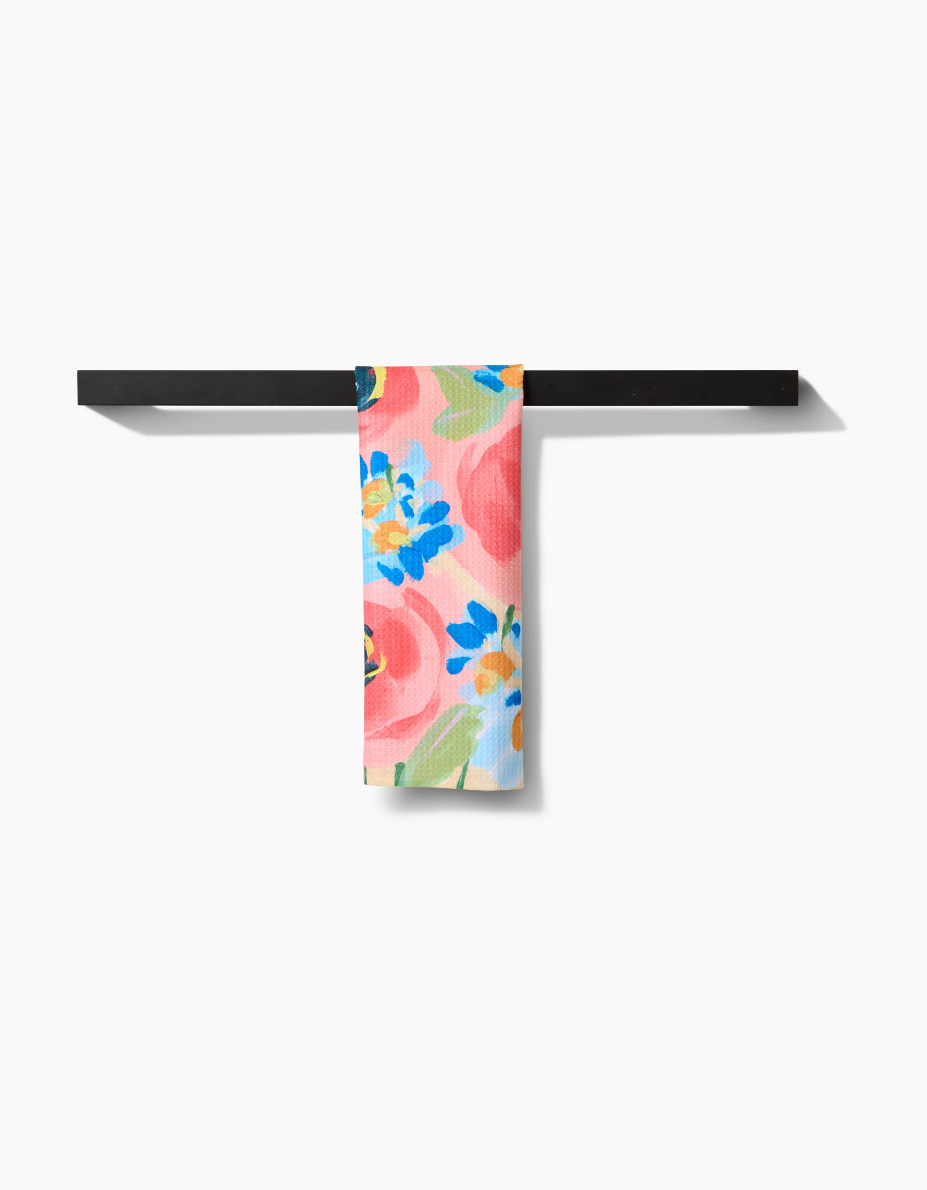 A sleek black bar displays the Margot bar towel by Ania Zwara Art, featuring bold pink, yellow, and blue flowers on Geoweave fabric against a light background, set on a plain white backdrop.