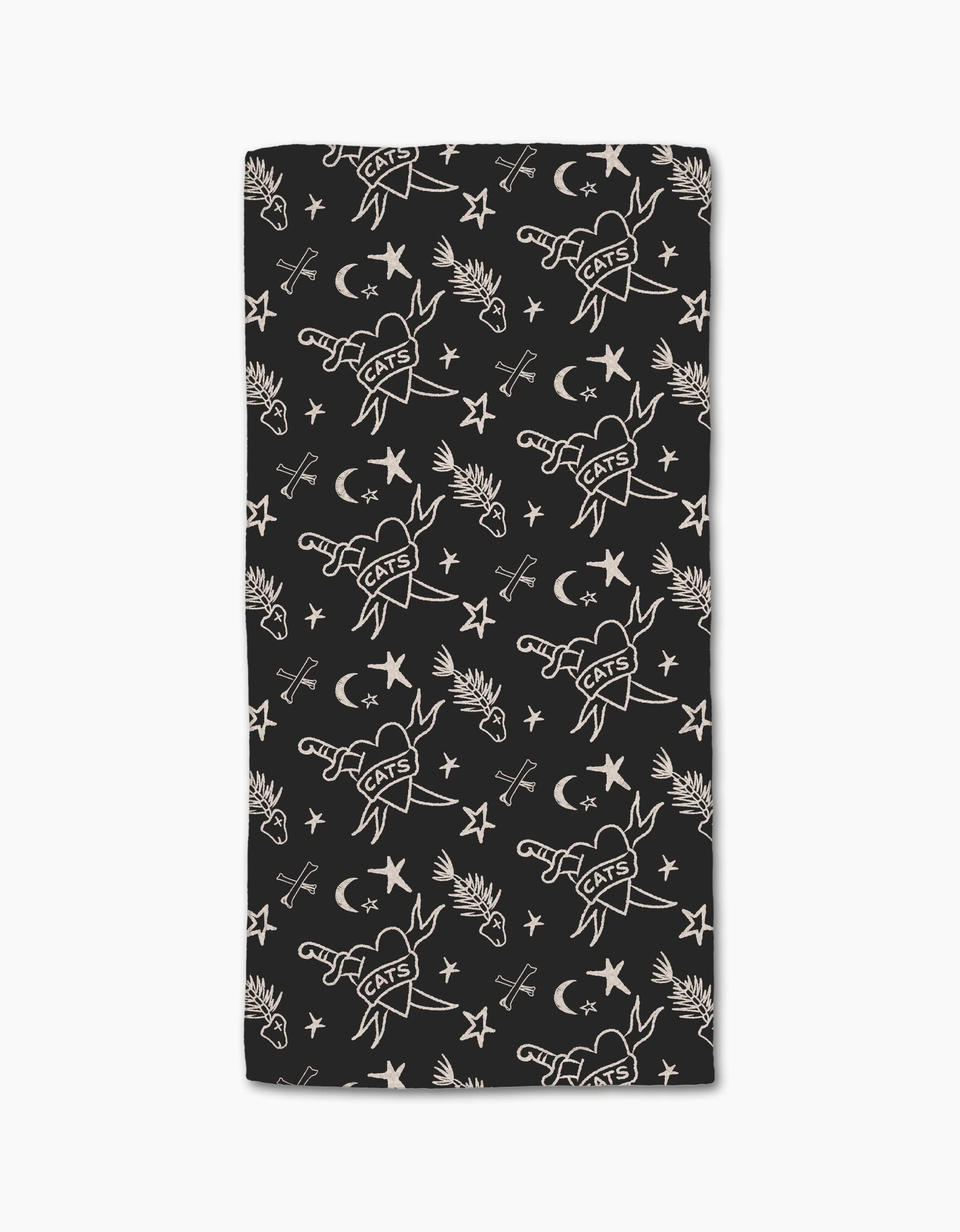 The Meow or Never bar towel by Cole Strem is a black, rectangular towel made from post-consumer recycled materials. It features white line art tattoo motifs—CATS hearts, birds, stars, moons, and flowers—on repeat.