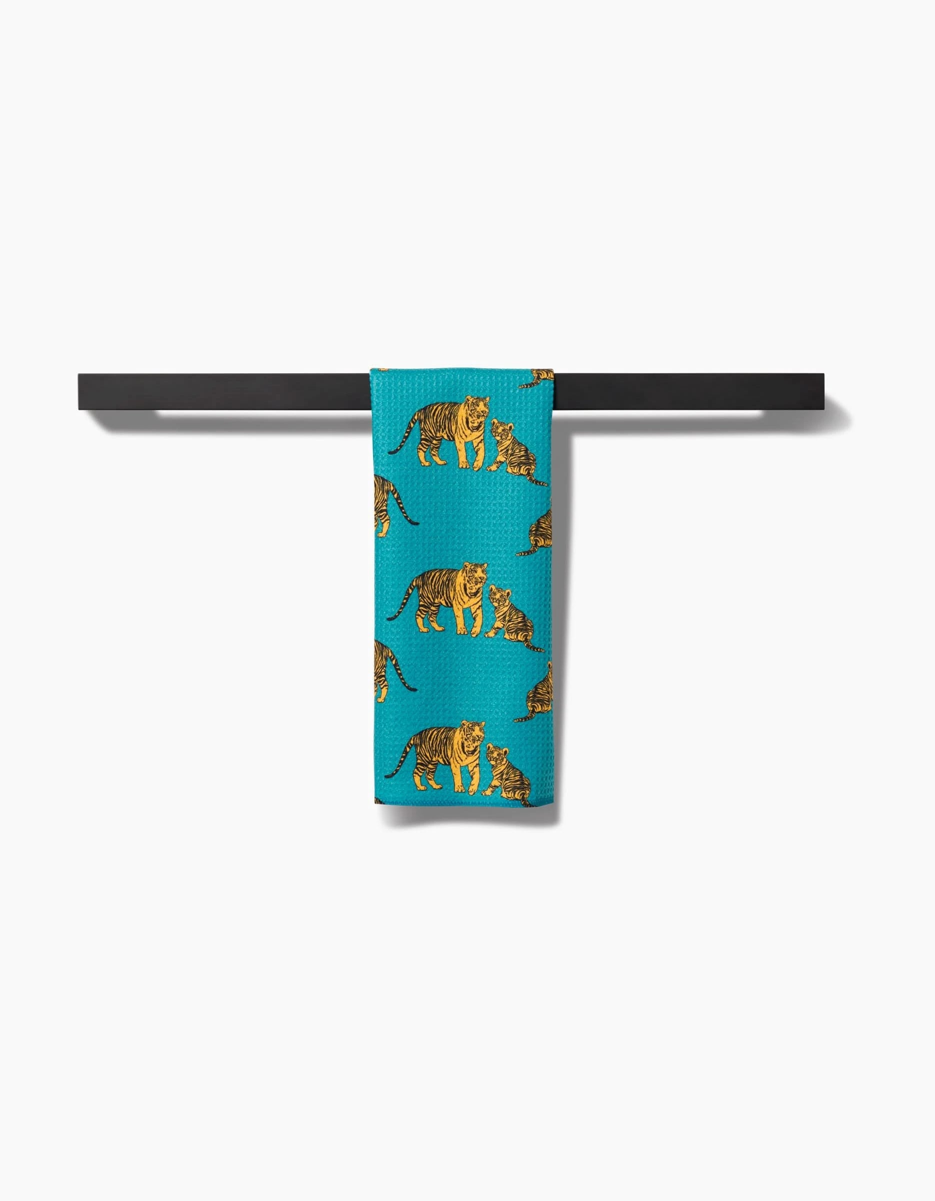 A Mommy and Me Bar Towel by Sarah Holden, crafted from Geoweave fabric and featuring repeated tiger illustrations in turquoise, hangs over a sleek black towel bar against a plain white background.