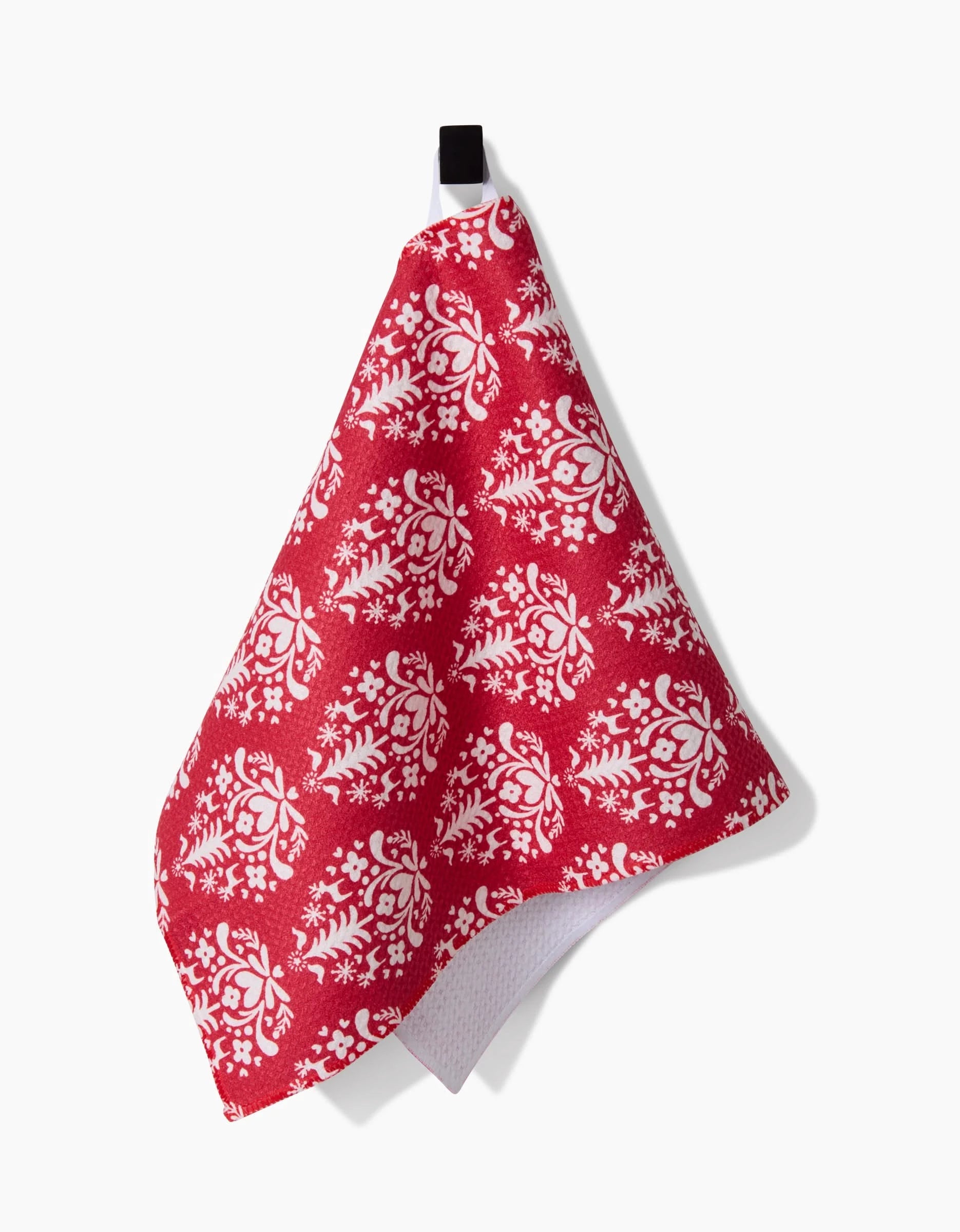 The Kayla Ann Nordic Holiday Stamp Red towel, featuring a white floral pattern, hangs from a black loop against a plain white background.