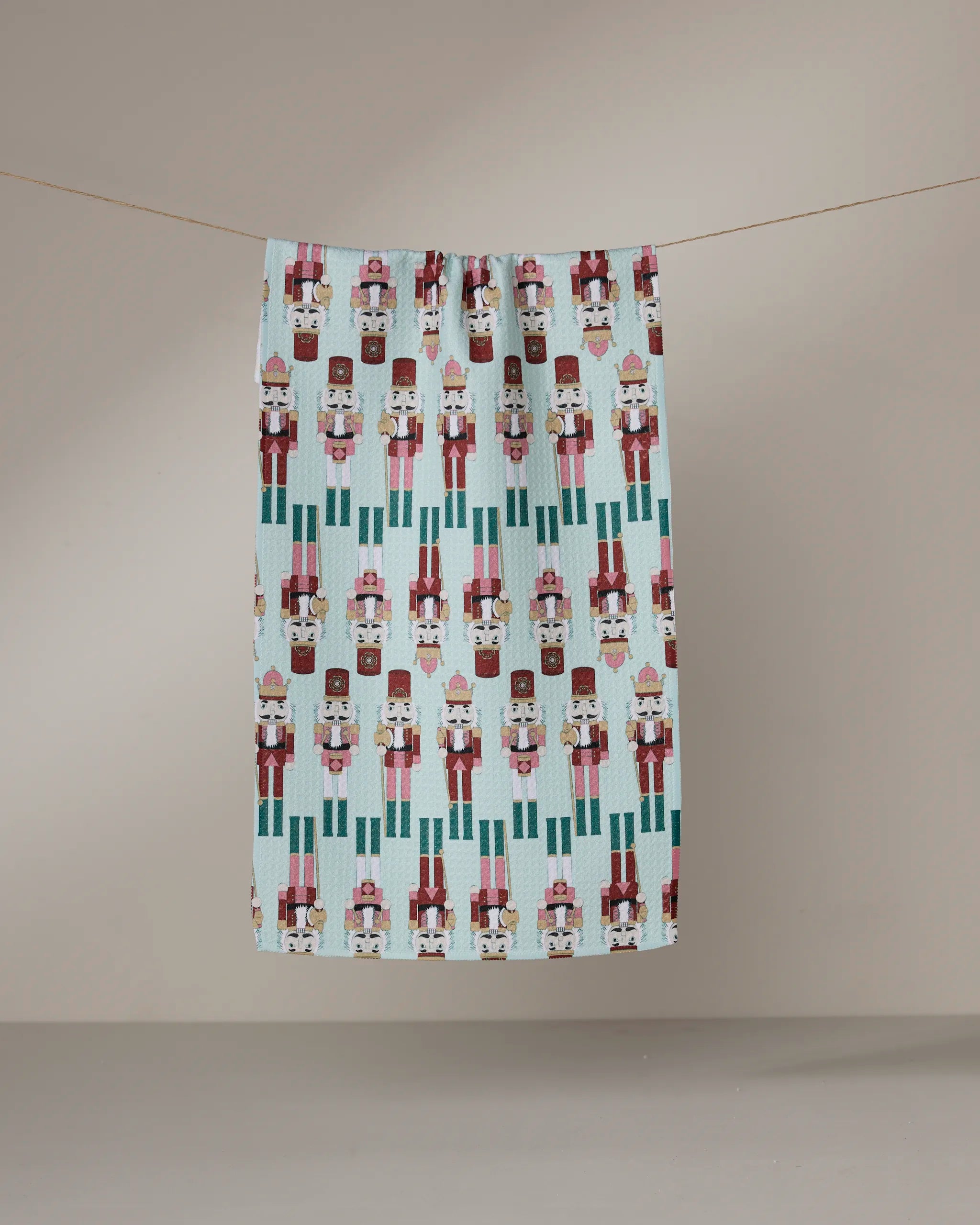Geometry’s Nutcracker March tea towel, featuring a colorful nutcracker soldier pattern and made from recycled materials, hangs on a clothesline against a plain beige background.