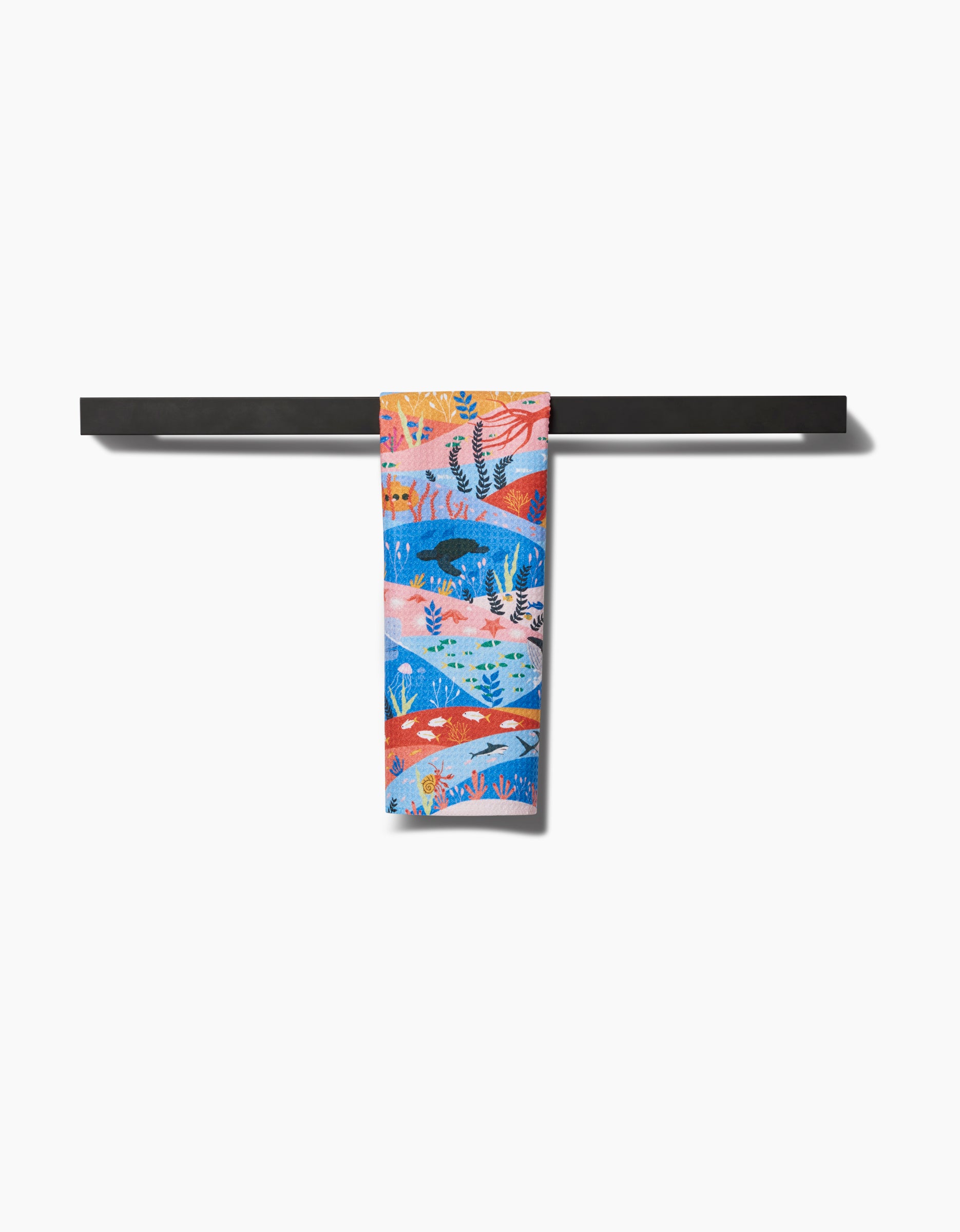 The Oceans Bar Towel by Ceyda Alasar features a vibrant abstract ocean-themed design with coral and fish. Made from recycled materials, it hangs neatly folded over a black towel bar for a stylish, eco-friendly touch to any space.