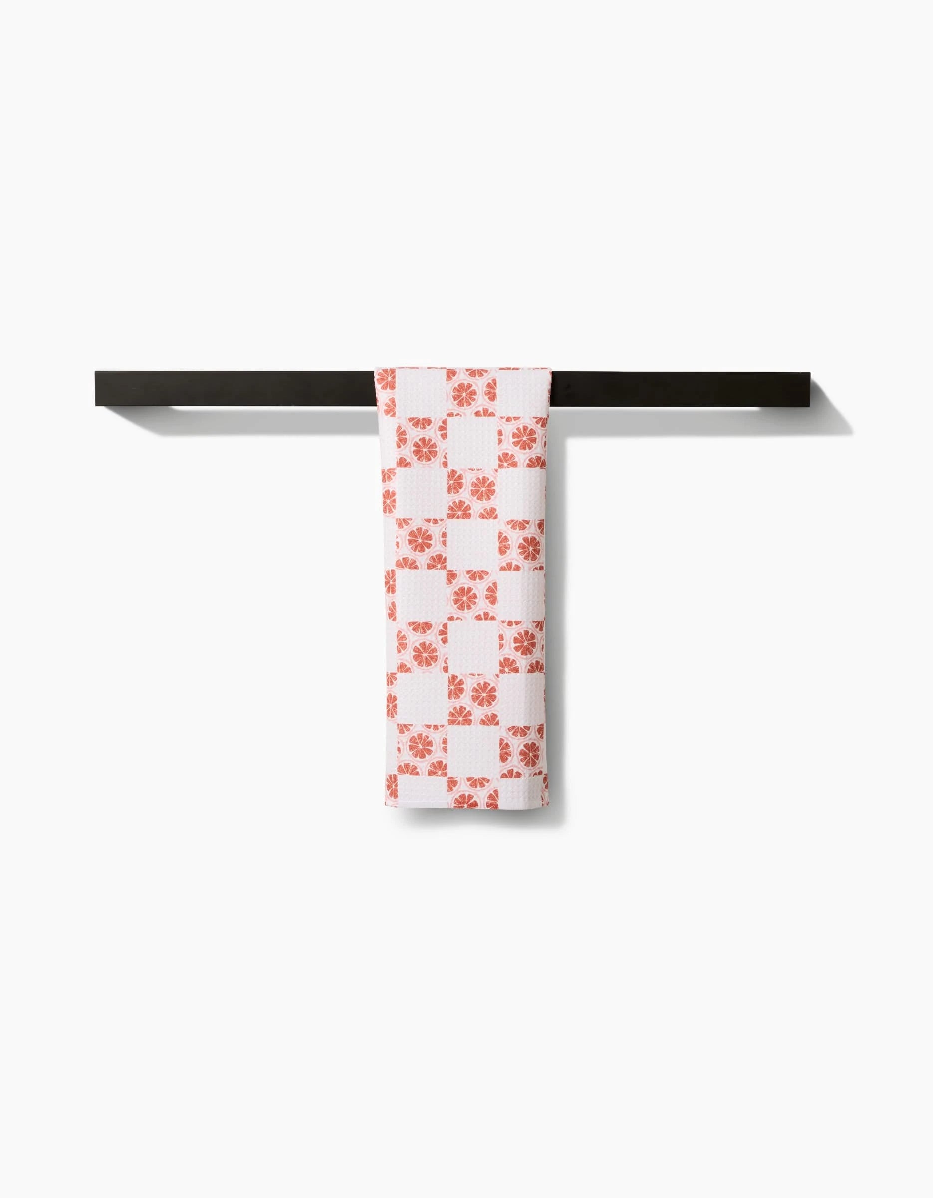 The Orange Checker by Teri the Butter, an orange checkered bar towel made from recycled materials, hangs neatly over a black towel bar against a plain white background.