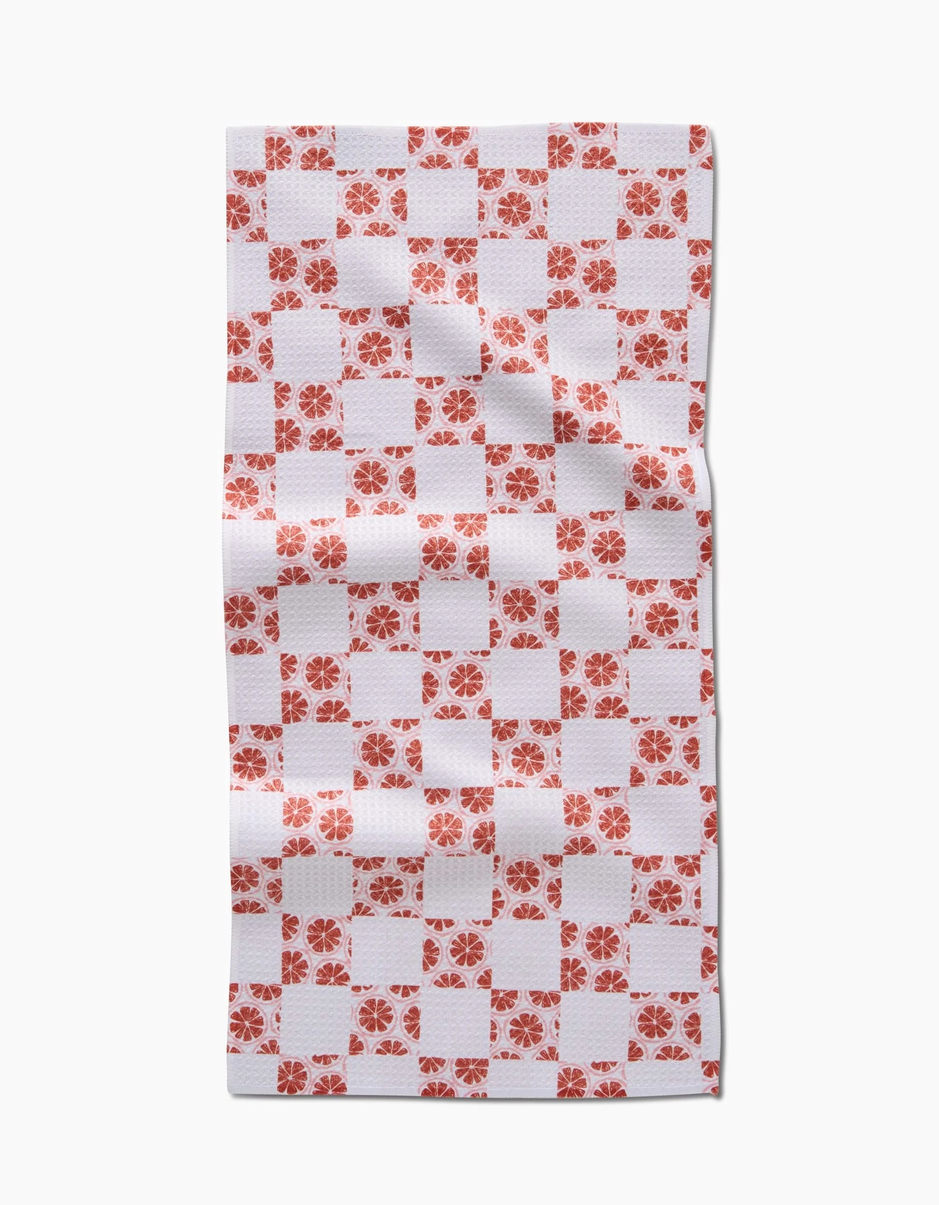 The Teri the Butter Orange Checker is a rectangular white cloth napkin with an orange checkerboard pattern and small orange floral designs in alternating squares, made from Geoweave fabric and shown laid flat with gentle wrinkles.