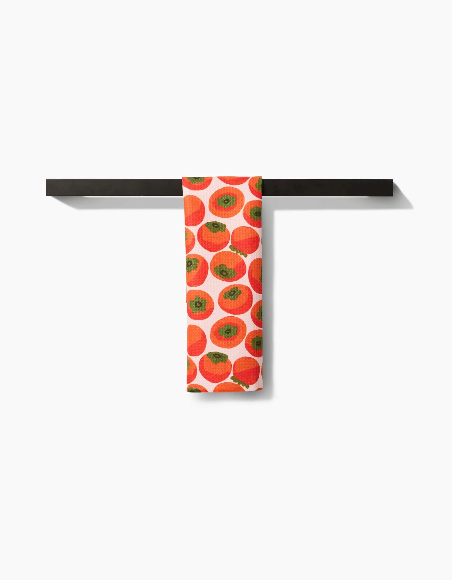 A Katie OShea Persimmons bar towel, made from Geoweave fabric and featuring a vibrant persimmon pattern, hangs neatly on a black bar against a white background.
