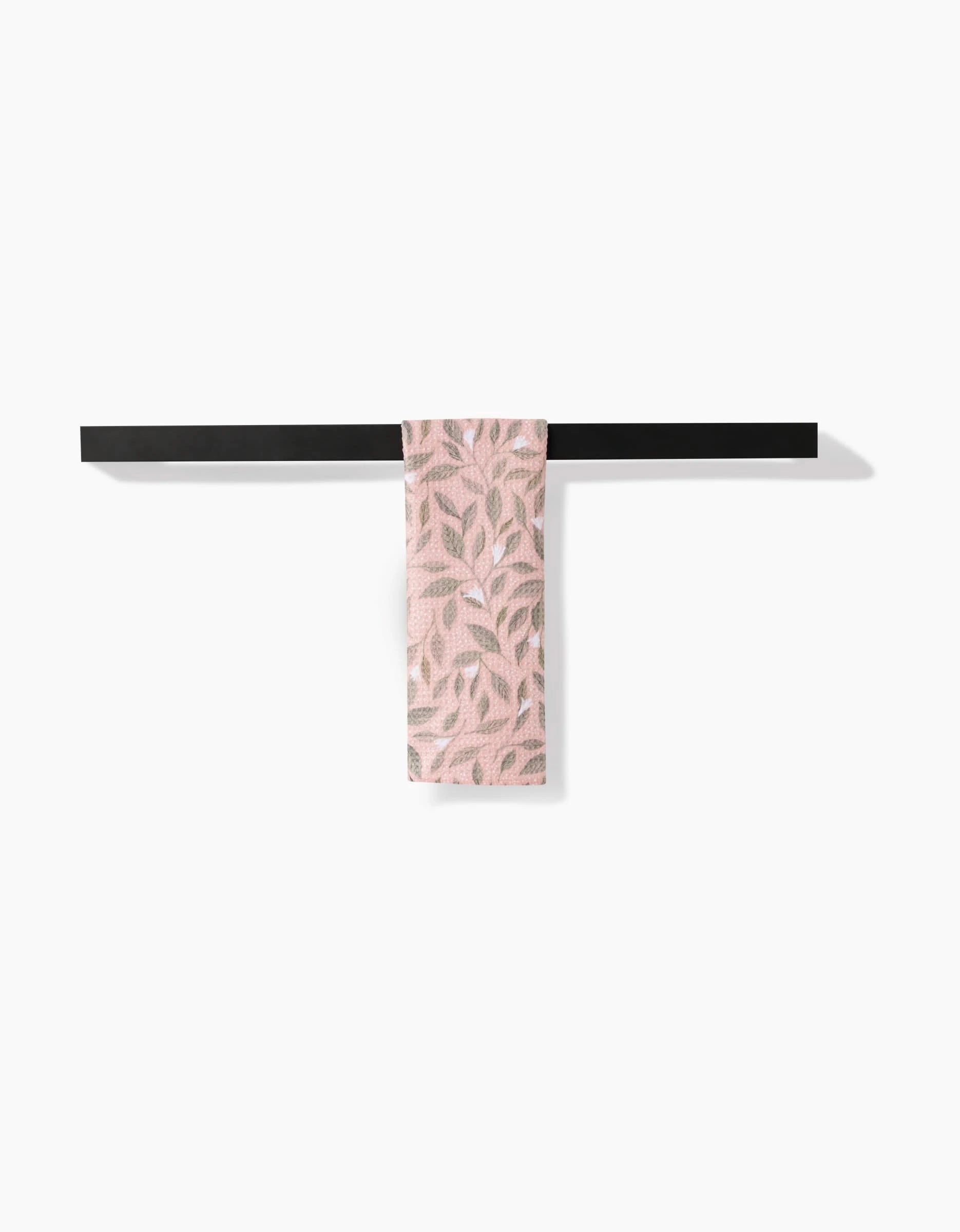 The Pink Mint Leaves bar towel by Katie OShea, featuring a leafy pattern and made from recycled materials, hangs on a black towel bar against a white background.