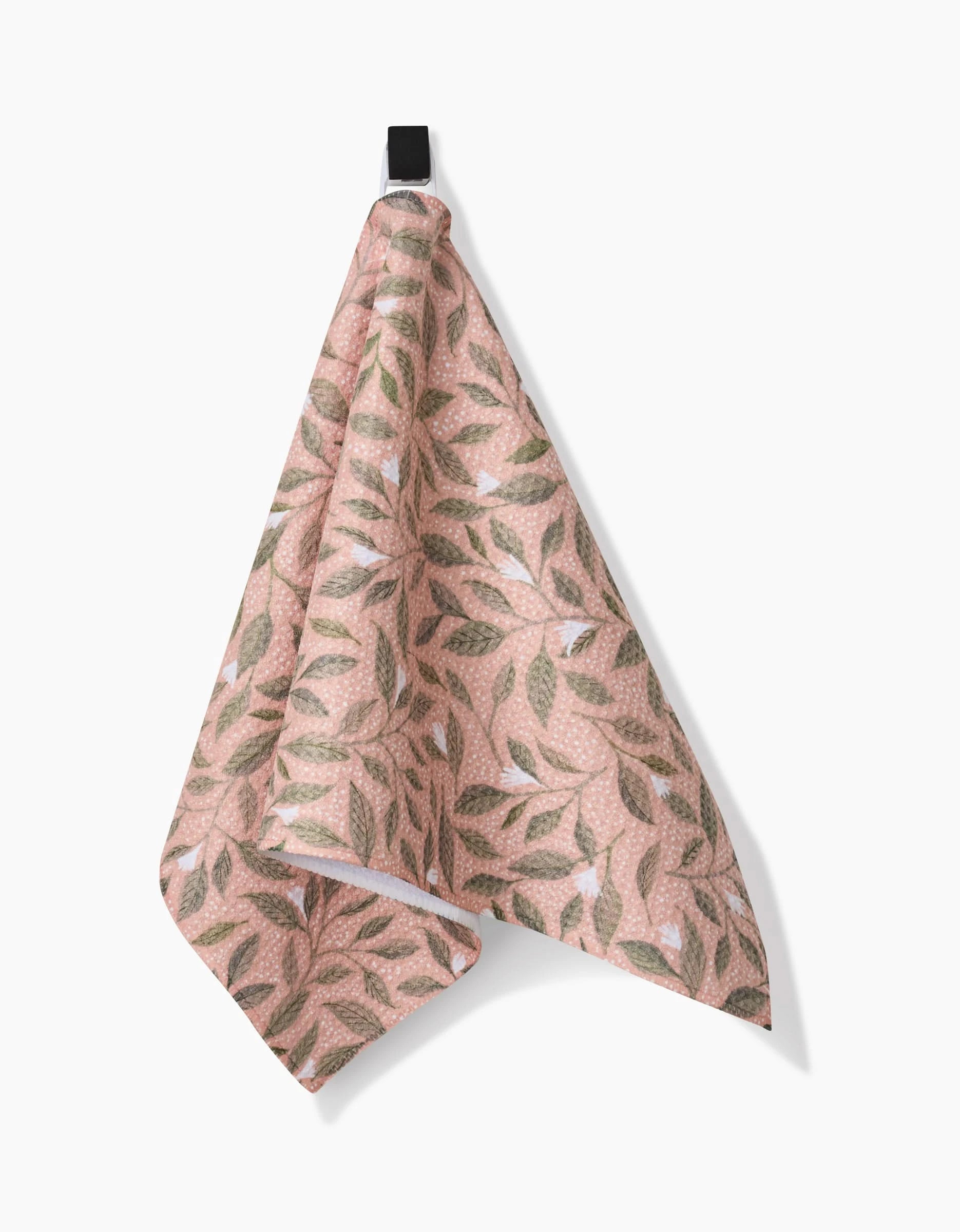 The Katie OShea Pink Mint Leaves bar towel, made from Geoweave fabric, features a green and brown leafy pattern on pink and hangs from a black loop against a white background.
